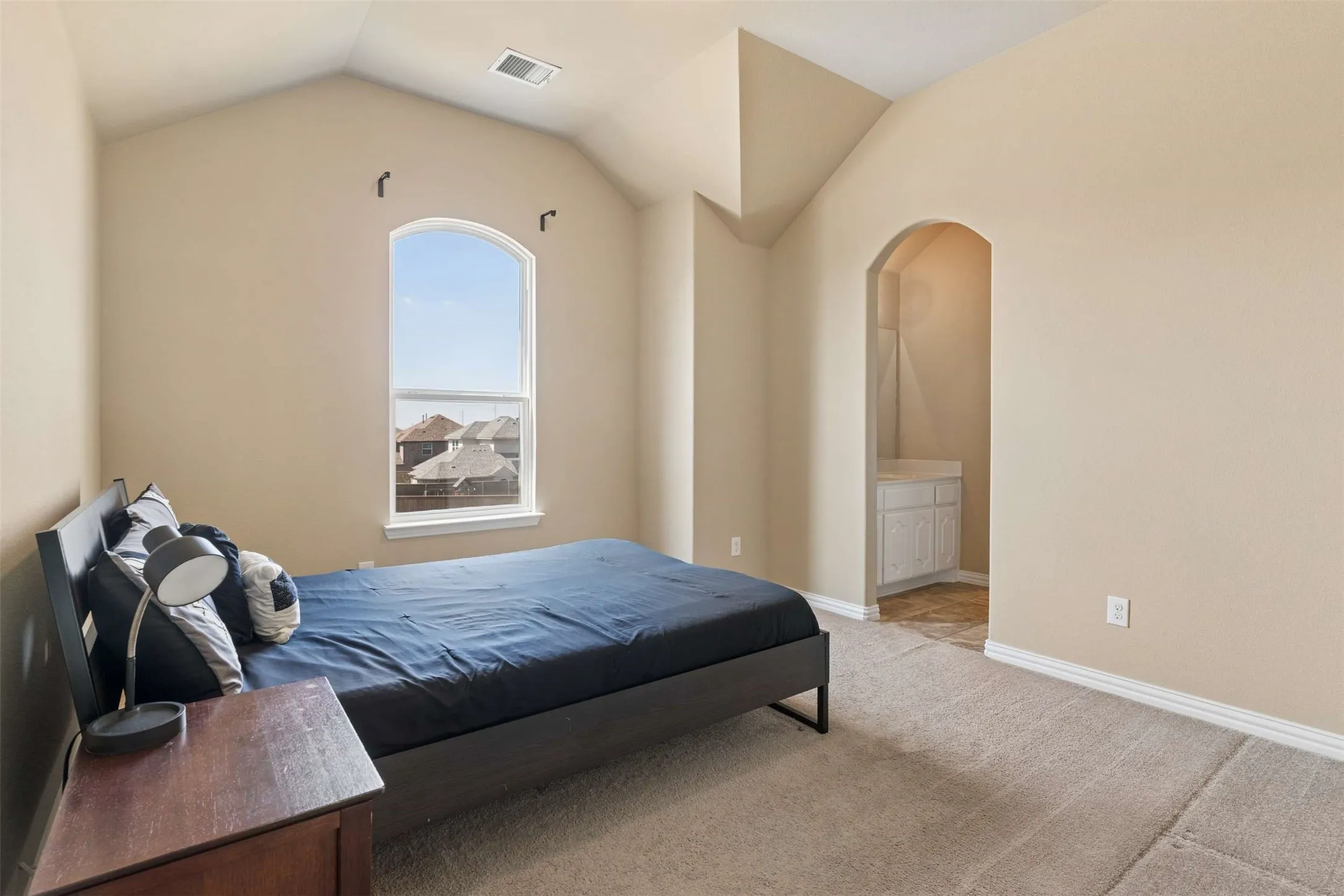 Bedroom featuring light colored carpet, arched walkways, ensuite bathroom, and vaulted ceiling