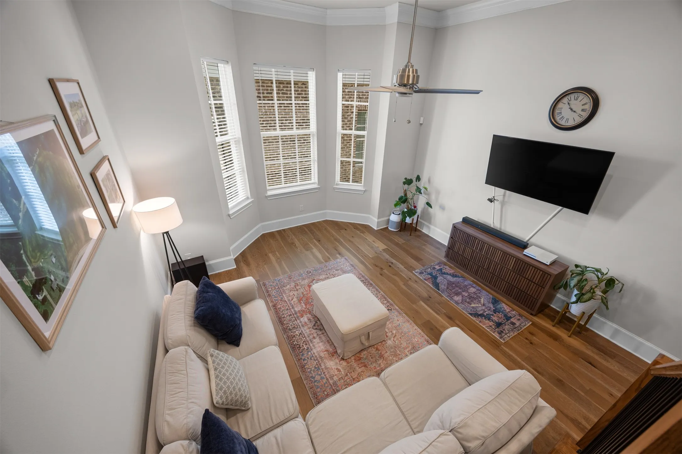 Bay window with three vertical windows, wood-finish flooring, ceiling fan, and crown molding