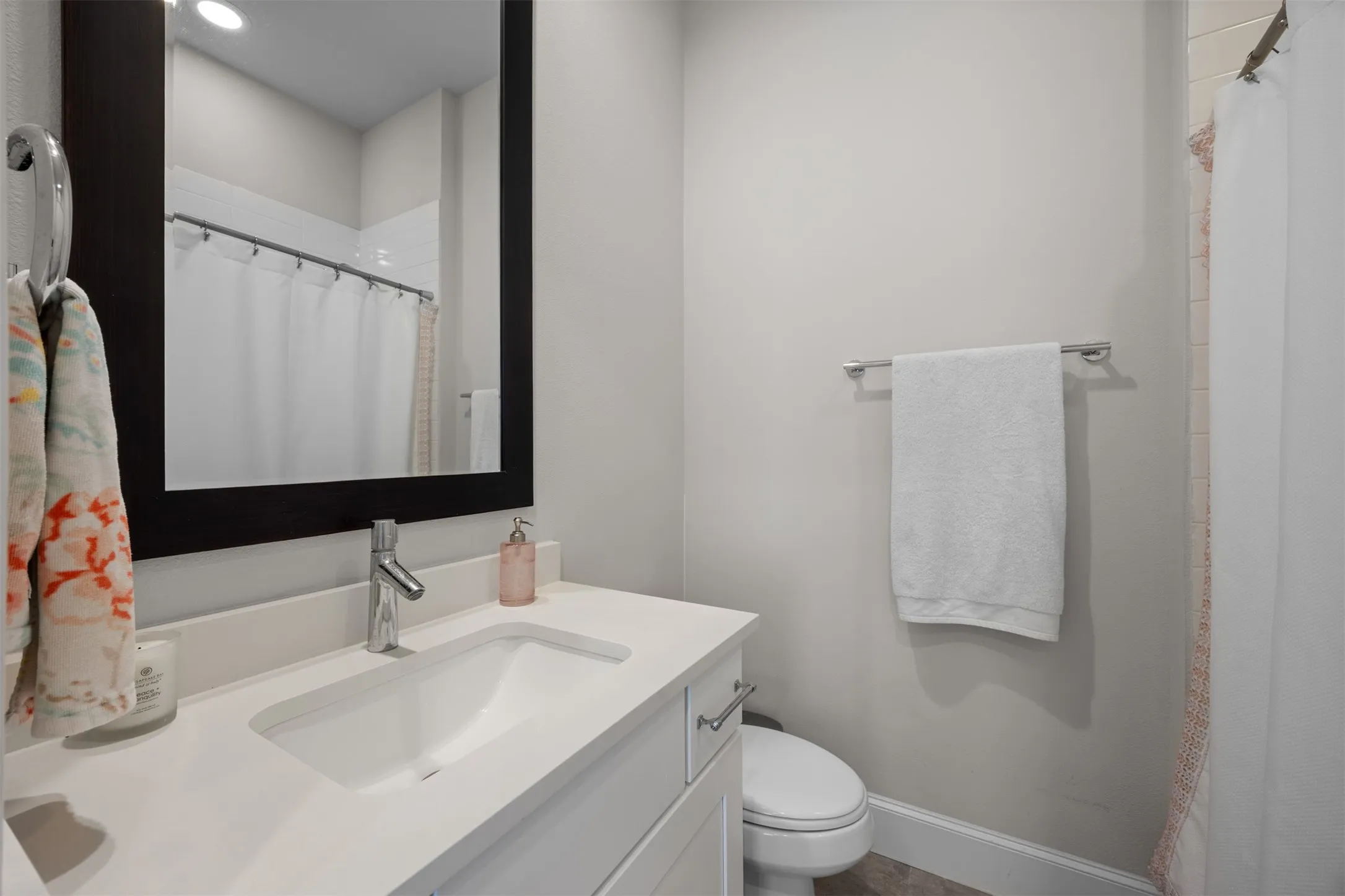 Modern vanity with an integrated sink and light-toned countertop, framed mirror, chrome-finish faucet, and white subway tile shower surround