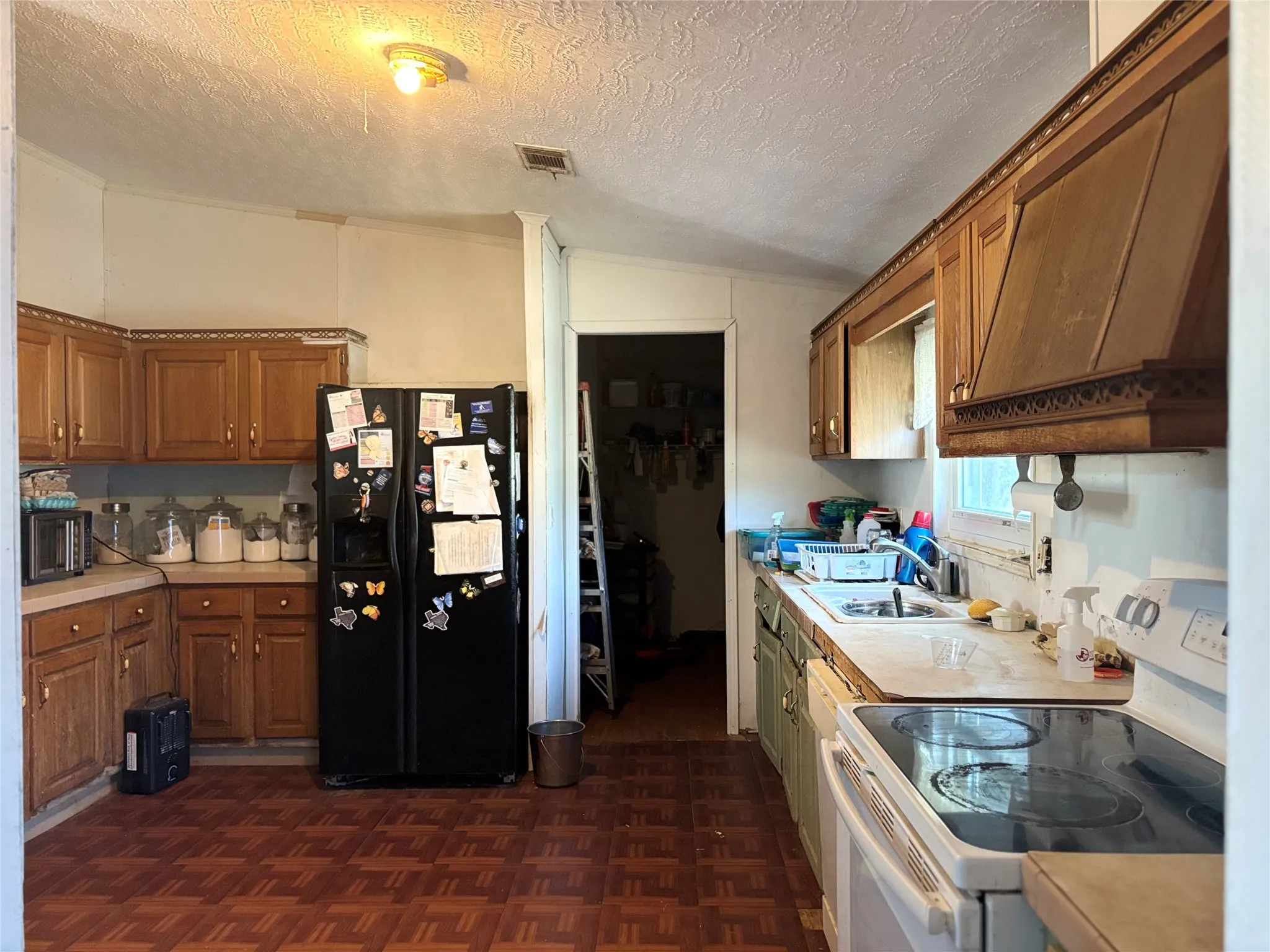 Kitchen with white electric stove, black fridge with ice dispenser, light countertops, a textured ceiling, and wood finish cabinetry