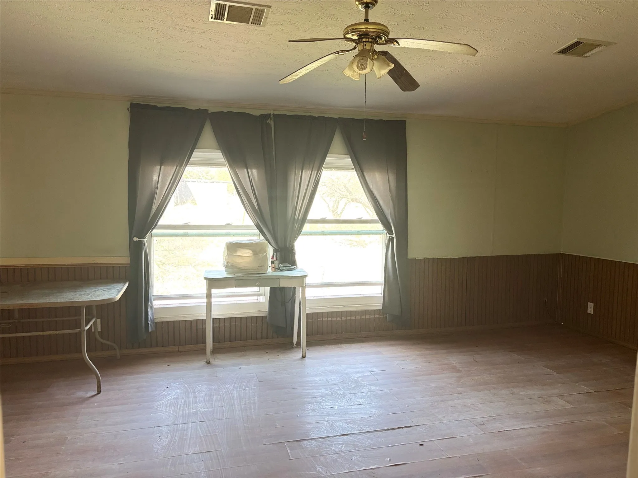 Empty room with a wainscoted wall, a ceiling fan, wood walls, a textured ceiling, and healthy amount of natural light