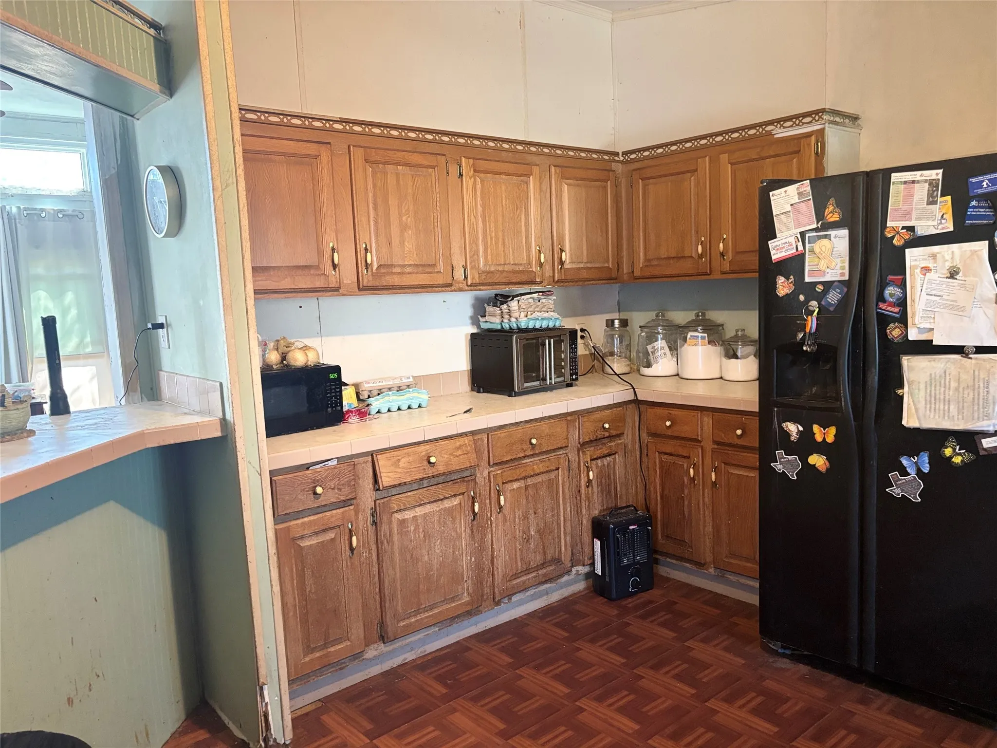 Kitchen with tile countertops, wood finish cabinetry, black appliances, and parquet floors