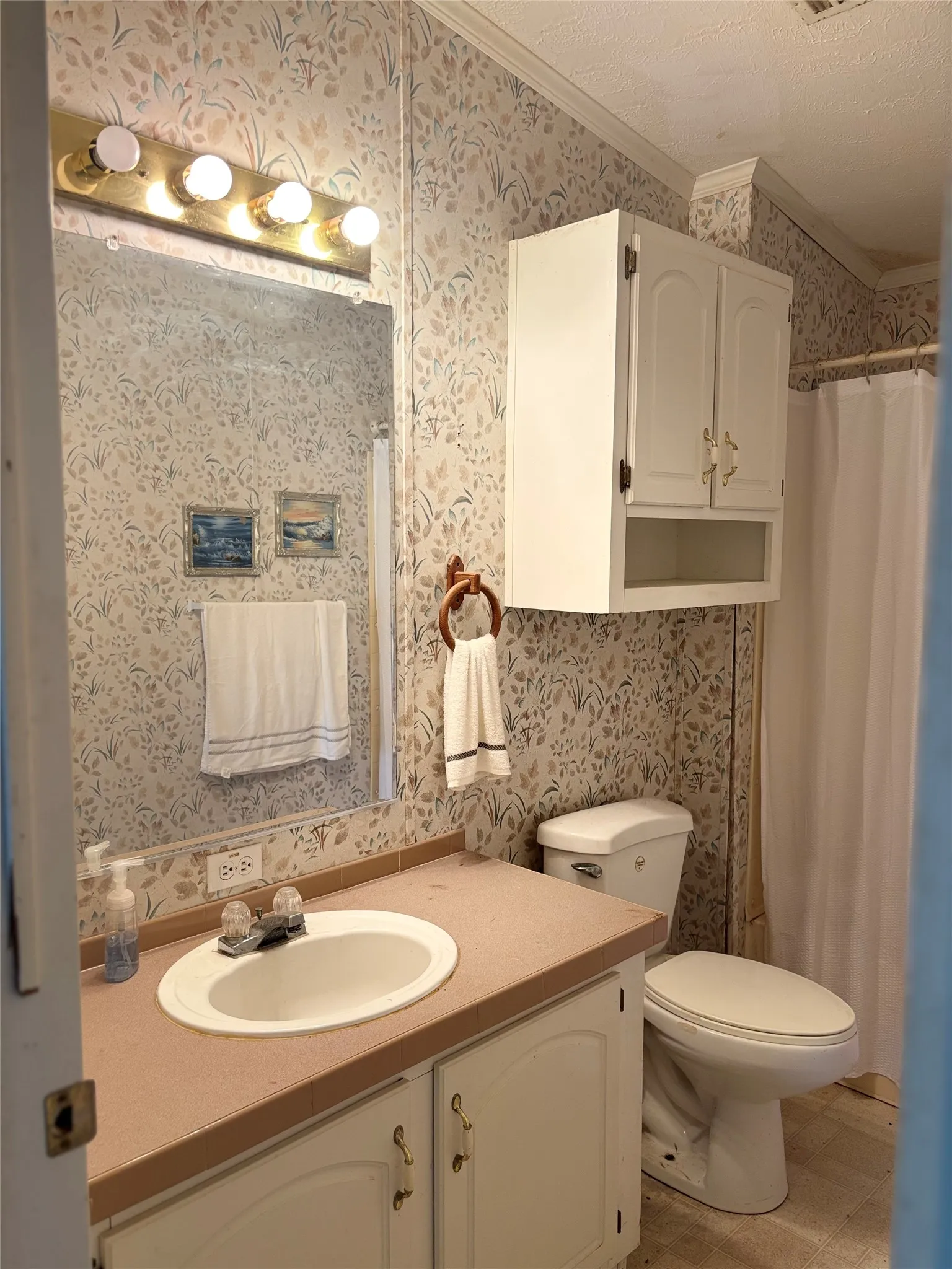Full bathroom featuring wallpapered walls, vanity, crown molding, a shower with shower curtain, and a textured ceiling