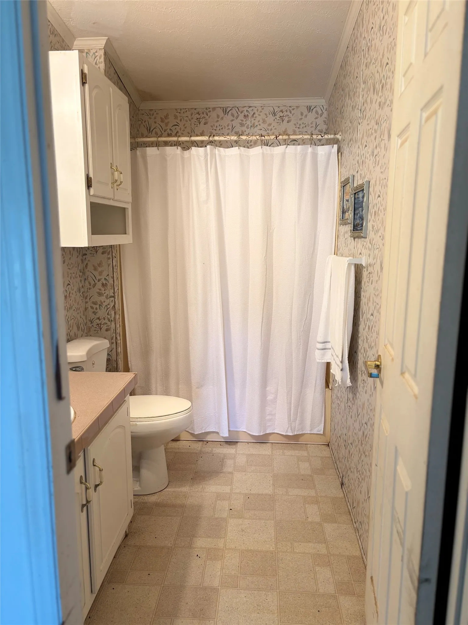 Bathroom with wallpapered walls, light floors, vanity, and ornamental molding