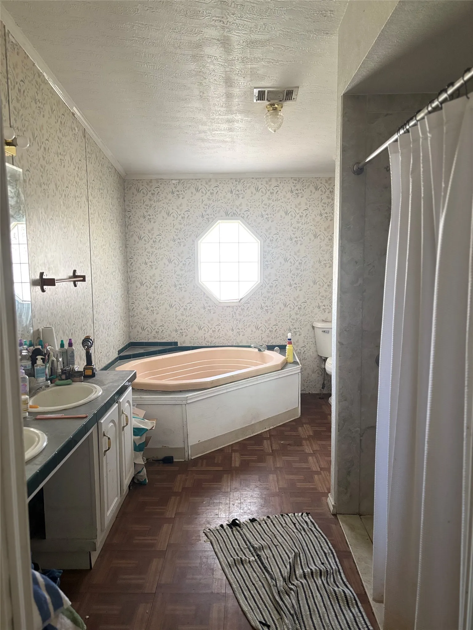 Bathroom featuring double vanity, wallpapered walls, a bath, a stall shower, and parquet floors