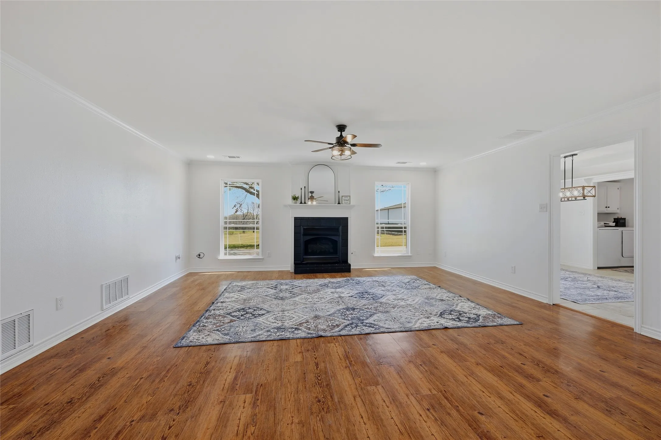 Unfurnished living room featuring ceiling fan, light wood-style flooring, crown molding, and a fireplace with flush hearth