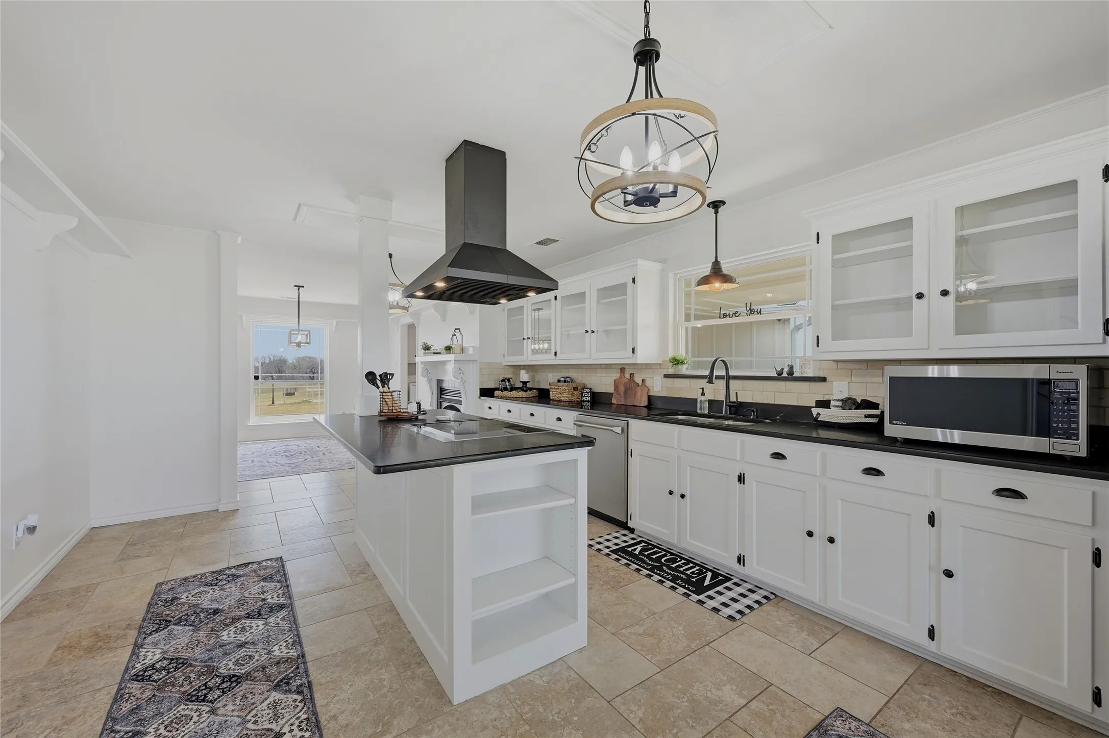 Kitchen featuring open shelves, suspended lighting, white cabinets, dark countertops, and a kitchen island with sink