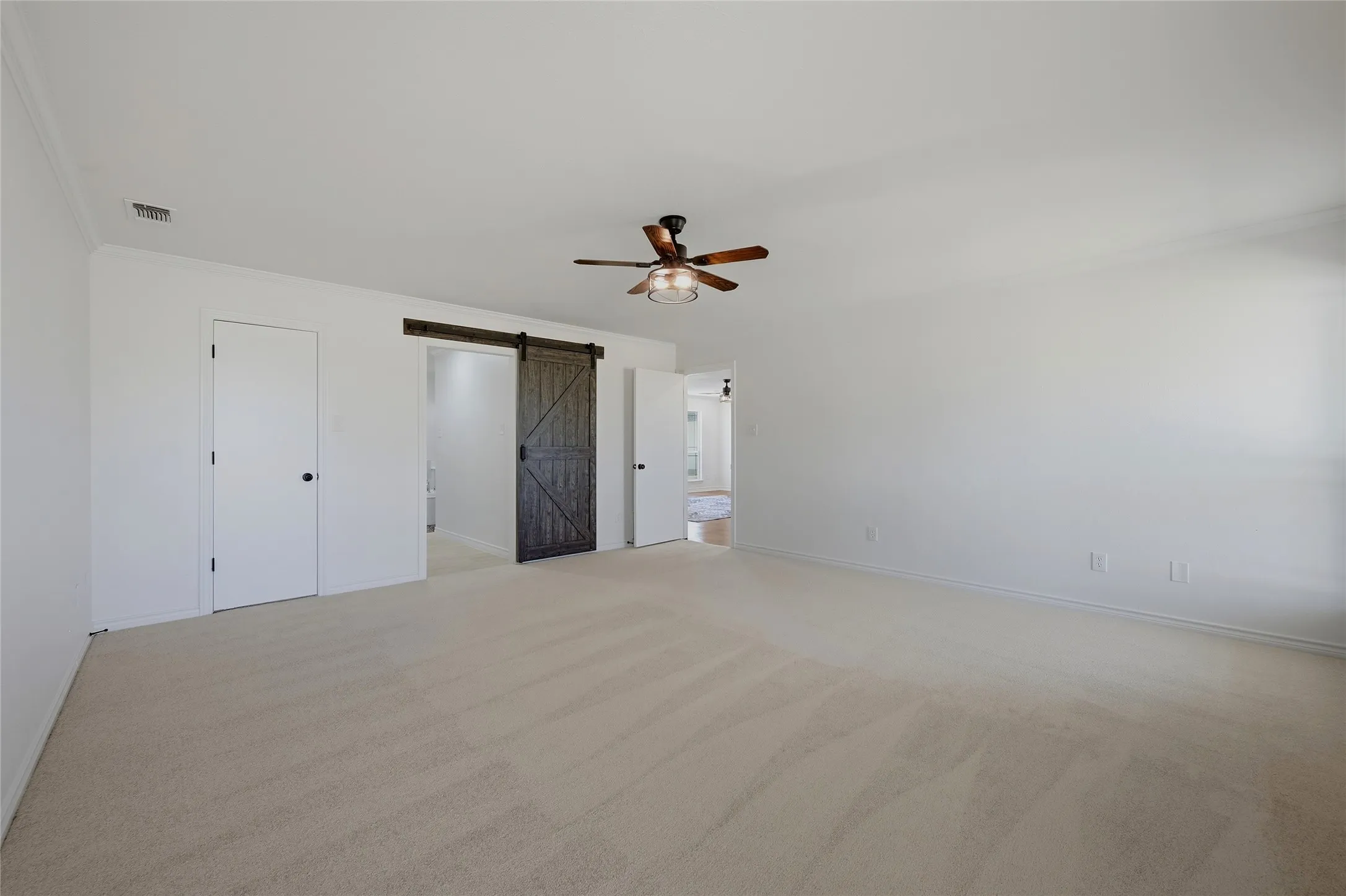 Unfurnished bedroom with crown molding, light carpet, a barn door, and a ceiling fan