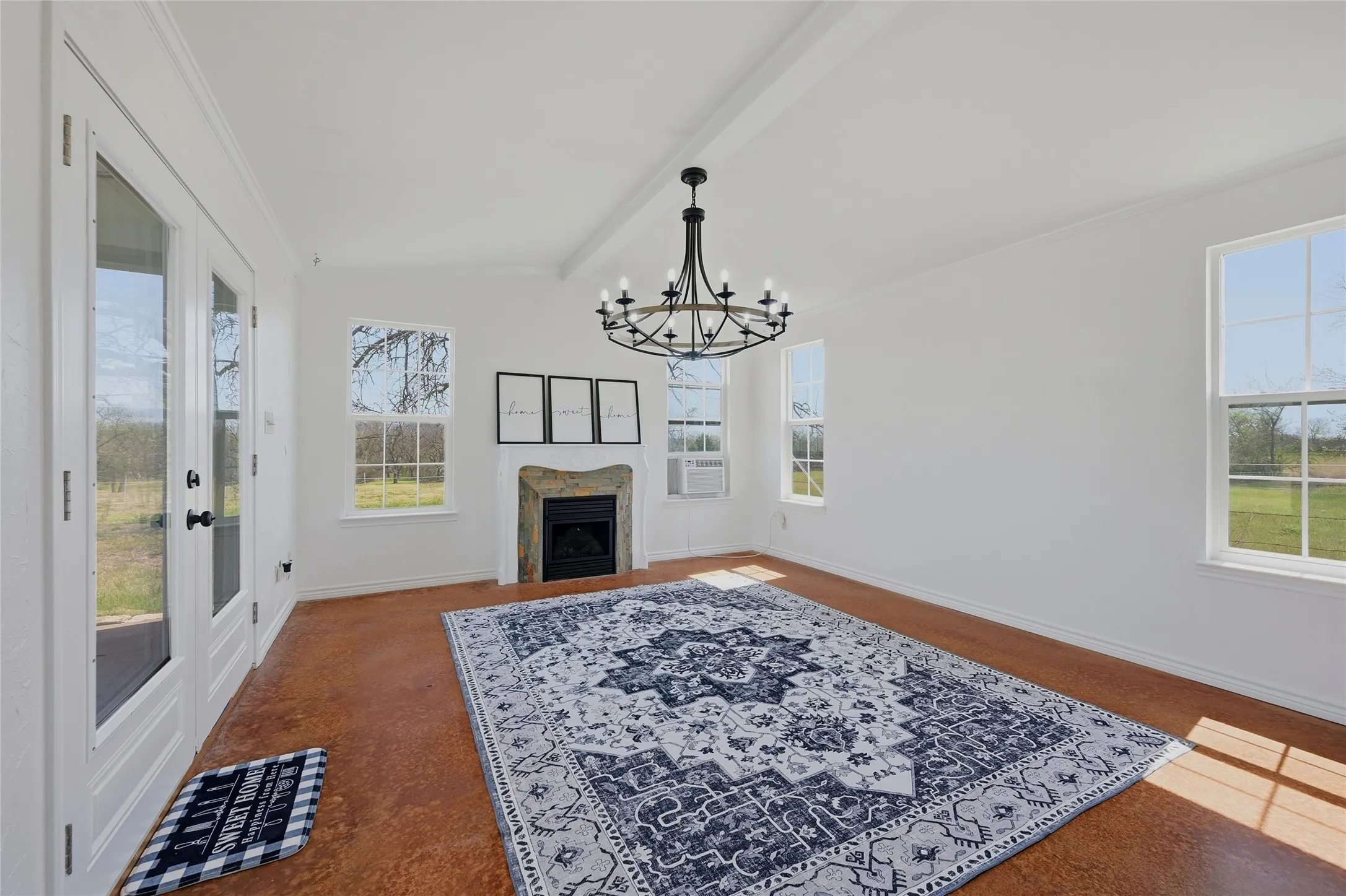 Living area featuring a fireplace, lofted ceiling with beams, suspended lighting, and plenty of natural light