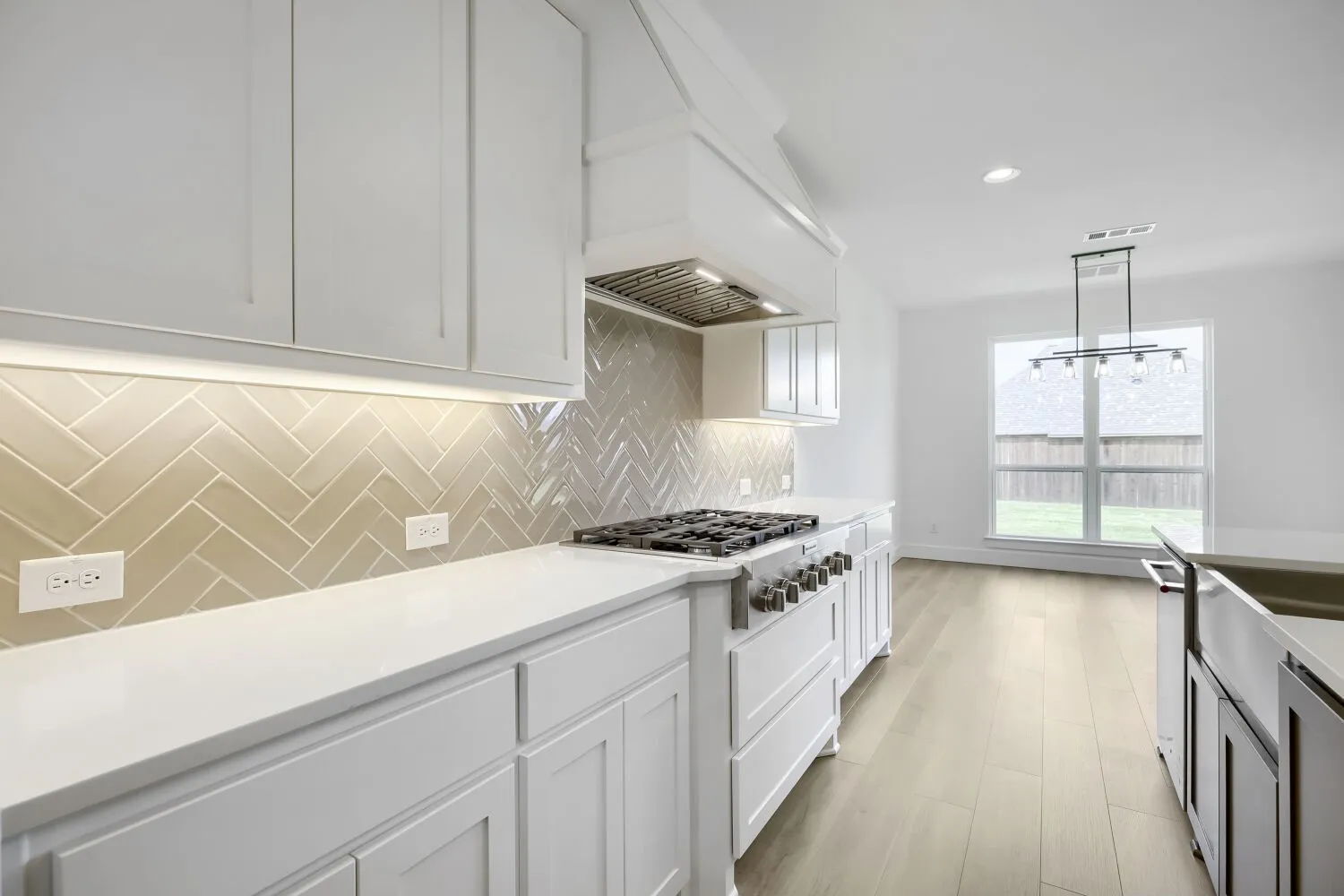 Modern kitchen featuring white shaker cabinetry, light-colored herringbone tile backsplash, white countertops, and wood-finish flooring