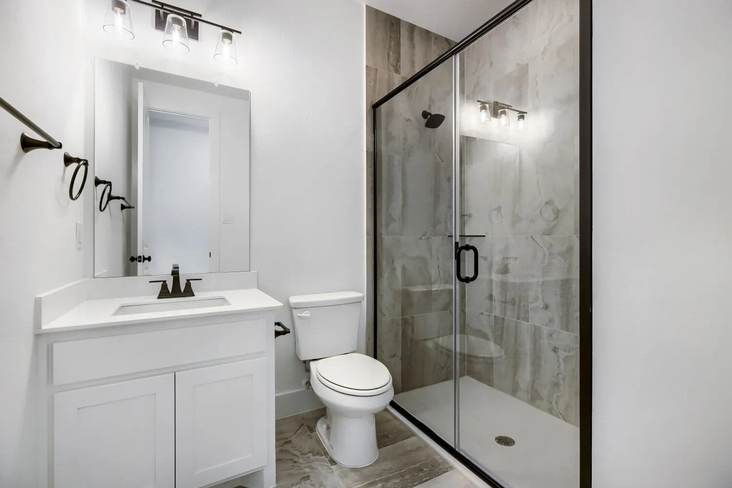 Contemporary bathroom featuring a frameless glass shower enclosure with matte black hardware, a white single vanity with a quartz countertop, and large format tile flooring