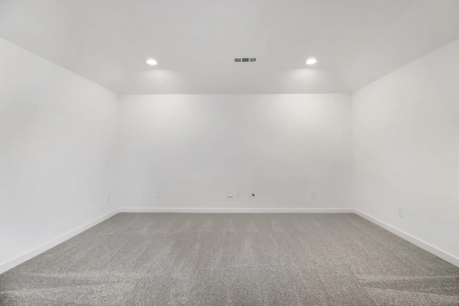 Spacious room featuring light gray carpeting, white walls, recessed ceiling lighting, and crisp baseboards