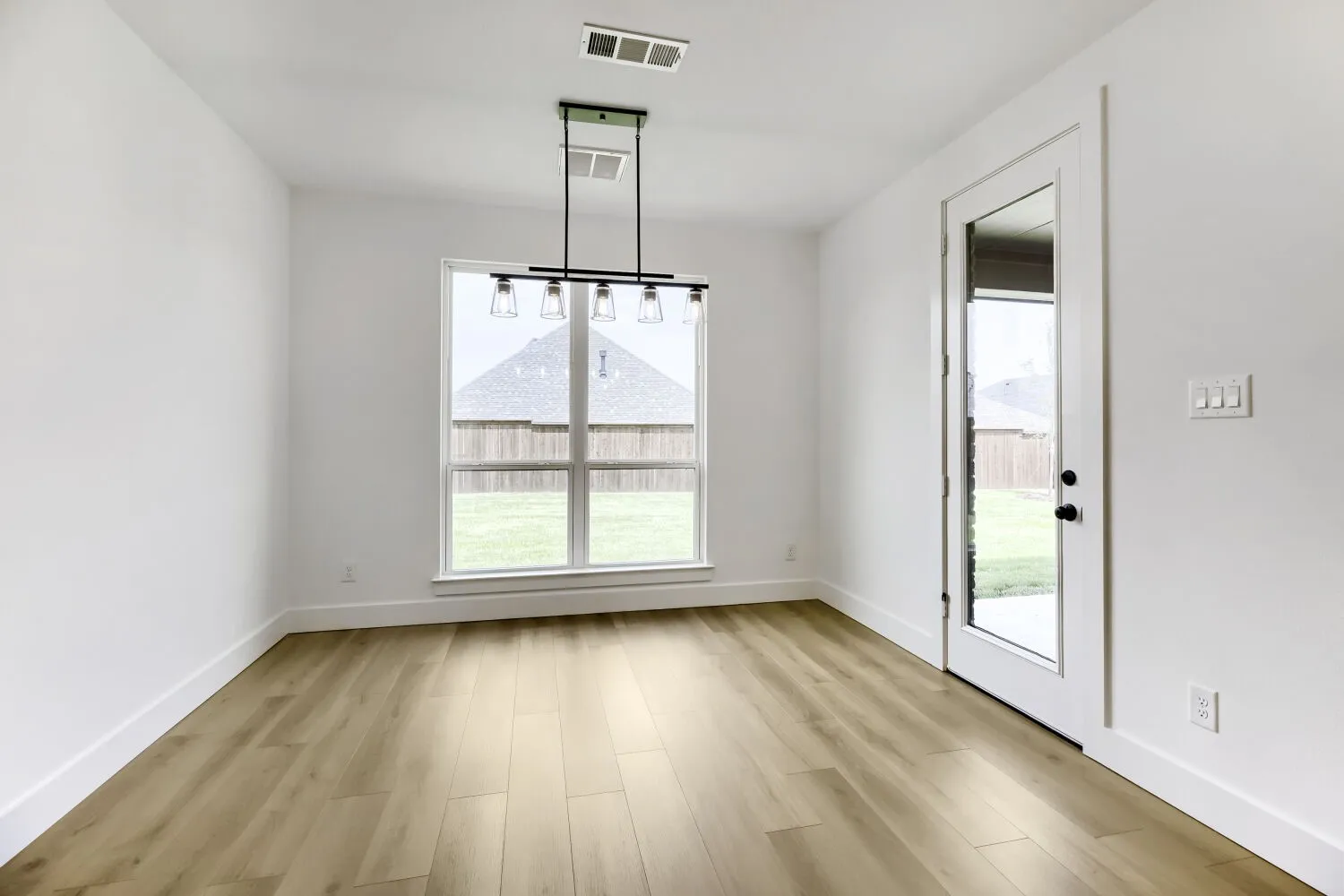 Dining area featuring wood-finish flooring, white walls, and a contemporary linear chandelier with five clear glass shades