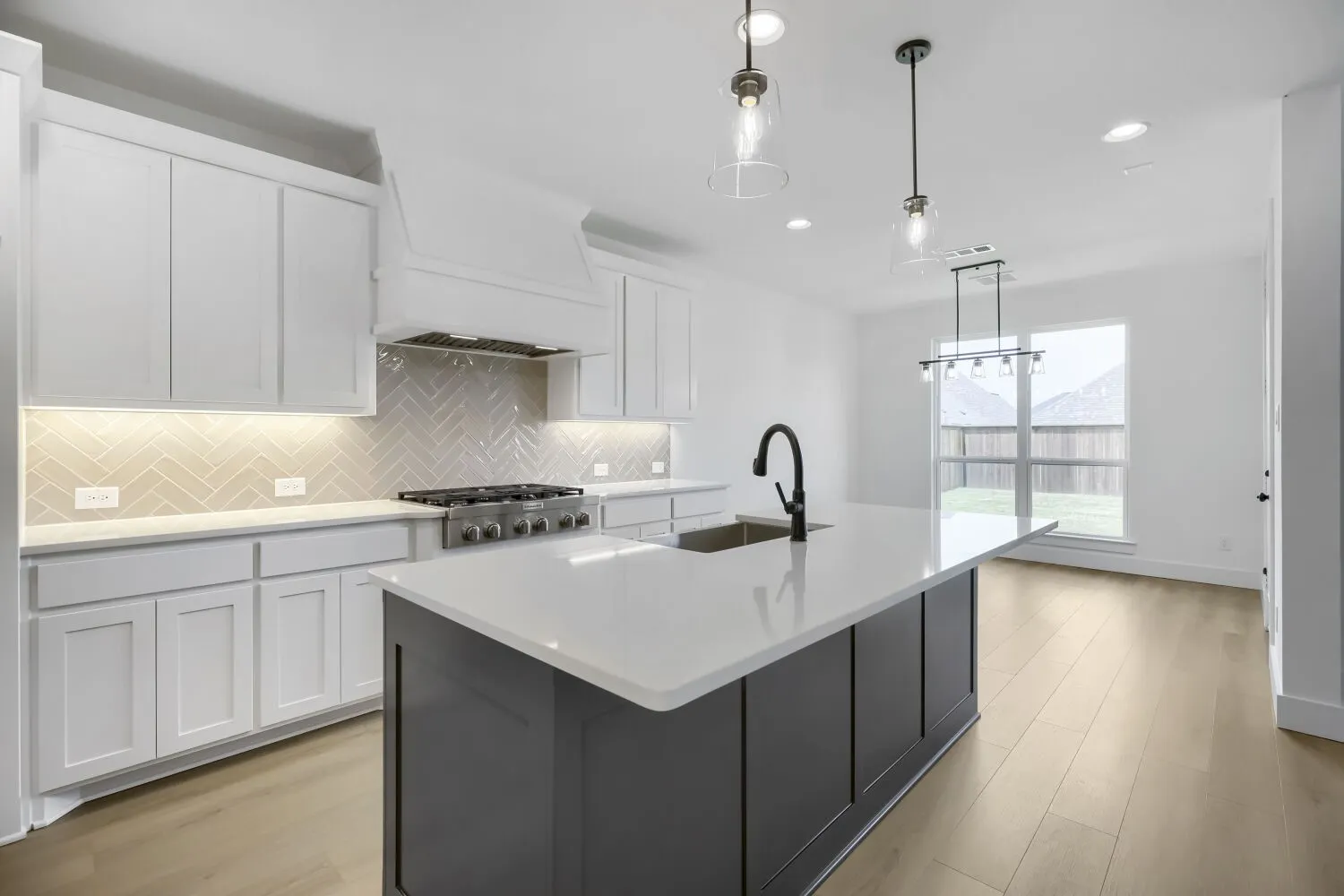 Kitchen featuring a large island with a surface, a stainless steel gas range, a chevron pattern backsplash, white shaker-style cabinetry, and wood-finish flooring