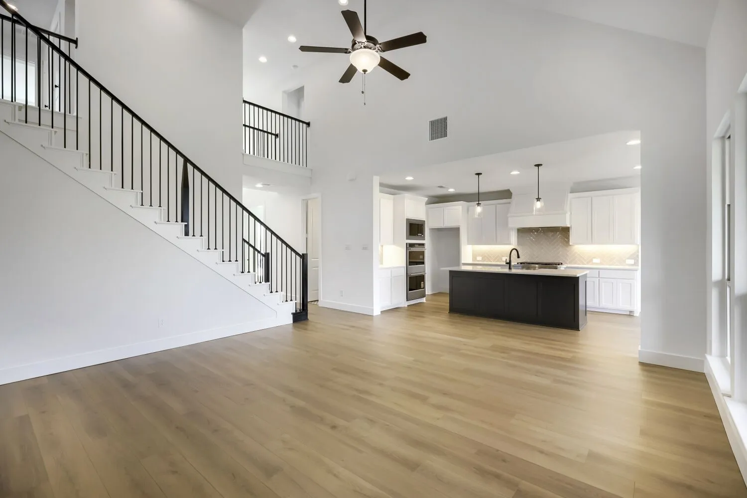 Open-concept living space with wood-finish flooring, a contemporary staircase featuring black iron balusters, and a vaulted ceiling