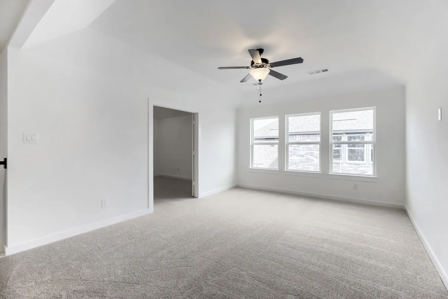 Spacious room featuring vaulted ceilings, light-hued carpeting, and a trio of windows providing ambient light