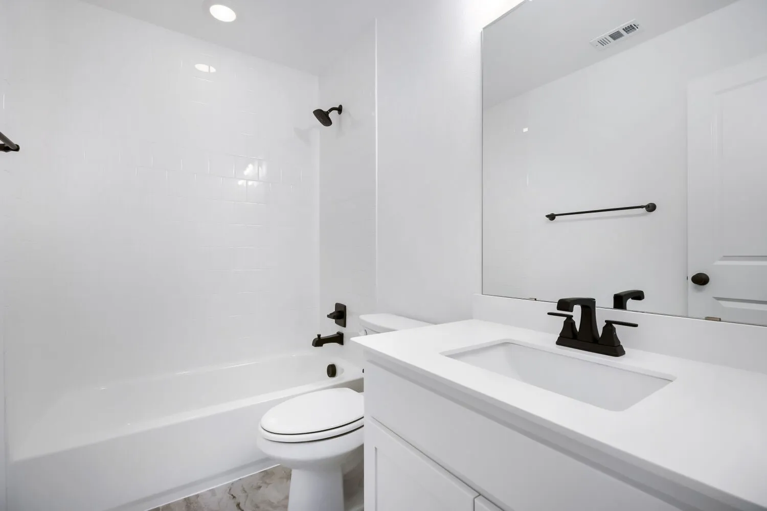 Bathroom featuring a white subway tile tub surround, white vanity with integrated sink, matte black fixtures, and a large wall-mounted mirror