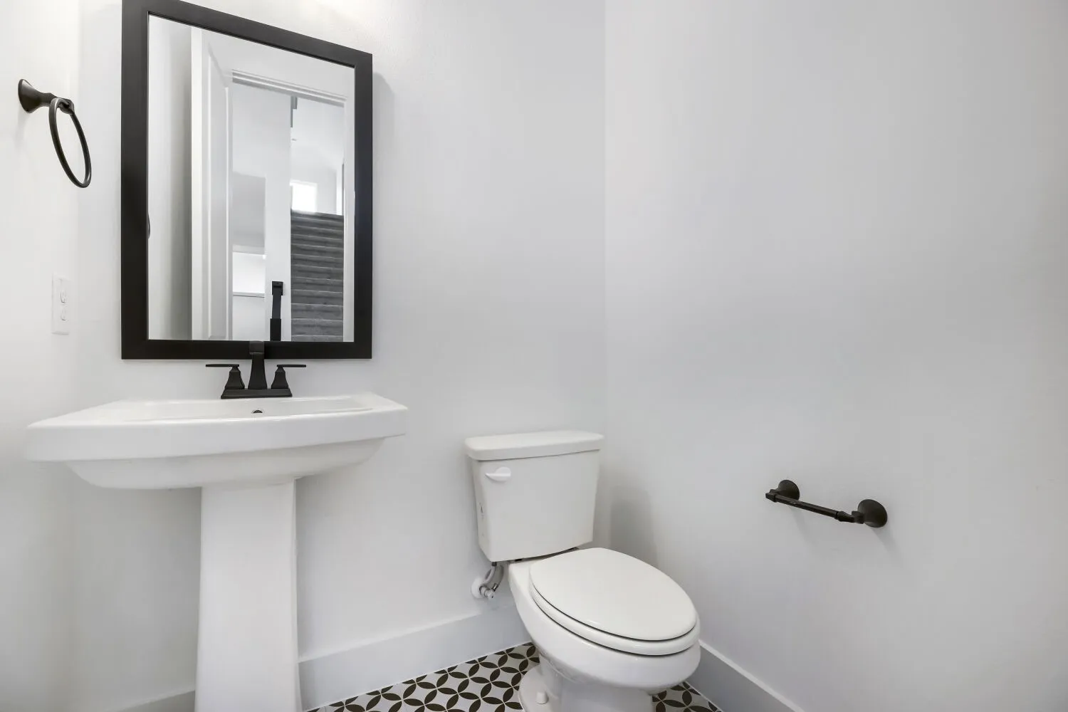 Modern powder room featuring a white pedestal sink with matte black faucet, a framed mirror, and a toilet
