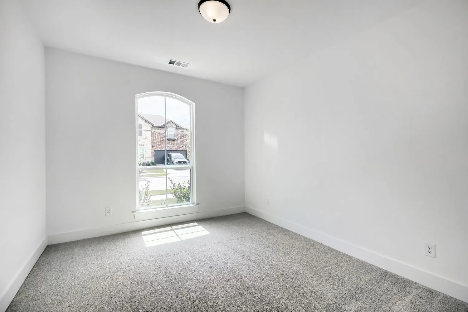 Bright room featuring an arched window, light gray carpet flooring, white walls, white baseboards, and a flush mount ceiling light fixture