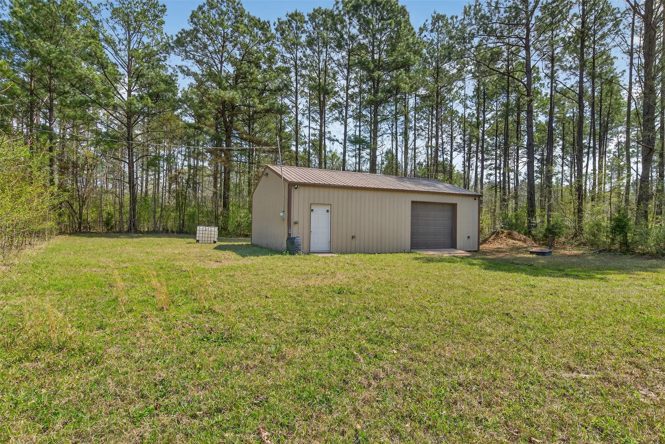 View of grassy yard with an outbuilding, a detached garage, and view of wooded area