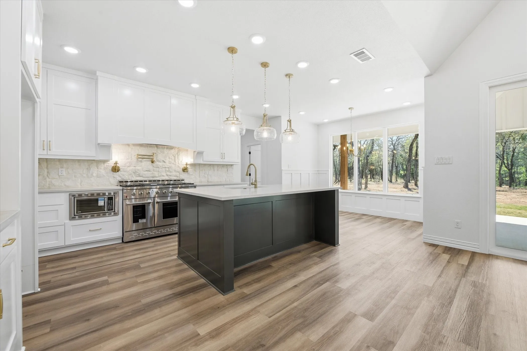 Two tone kitchen with stainless steel appliances, a center island with sink, pendant lighting, light stone countertops, and tasteful backsplash