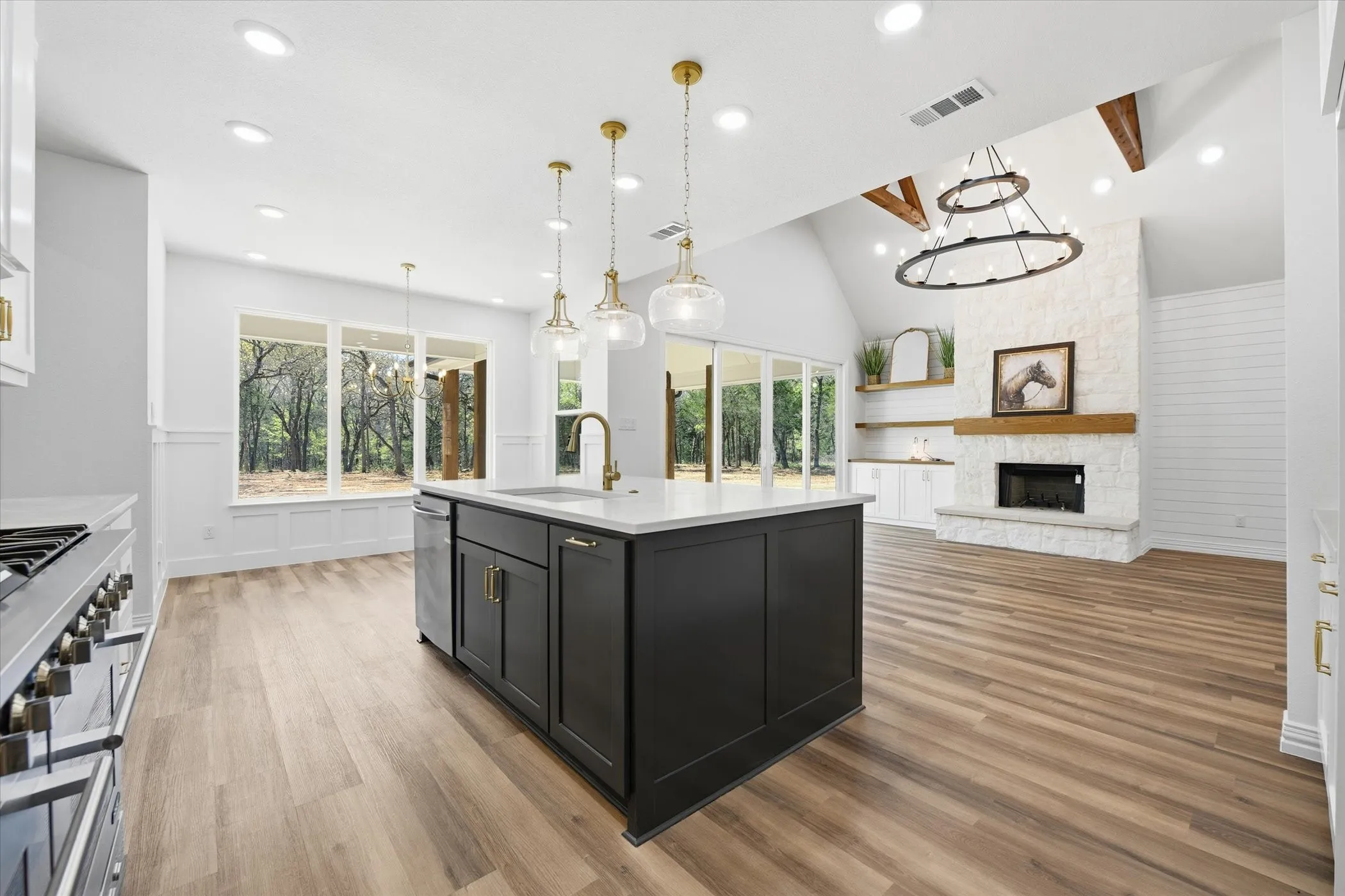 Kitchen with dark cabinetry, hanging lights, open floor plan, a stone fireplace, and stainless steel appliances