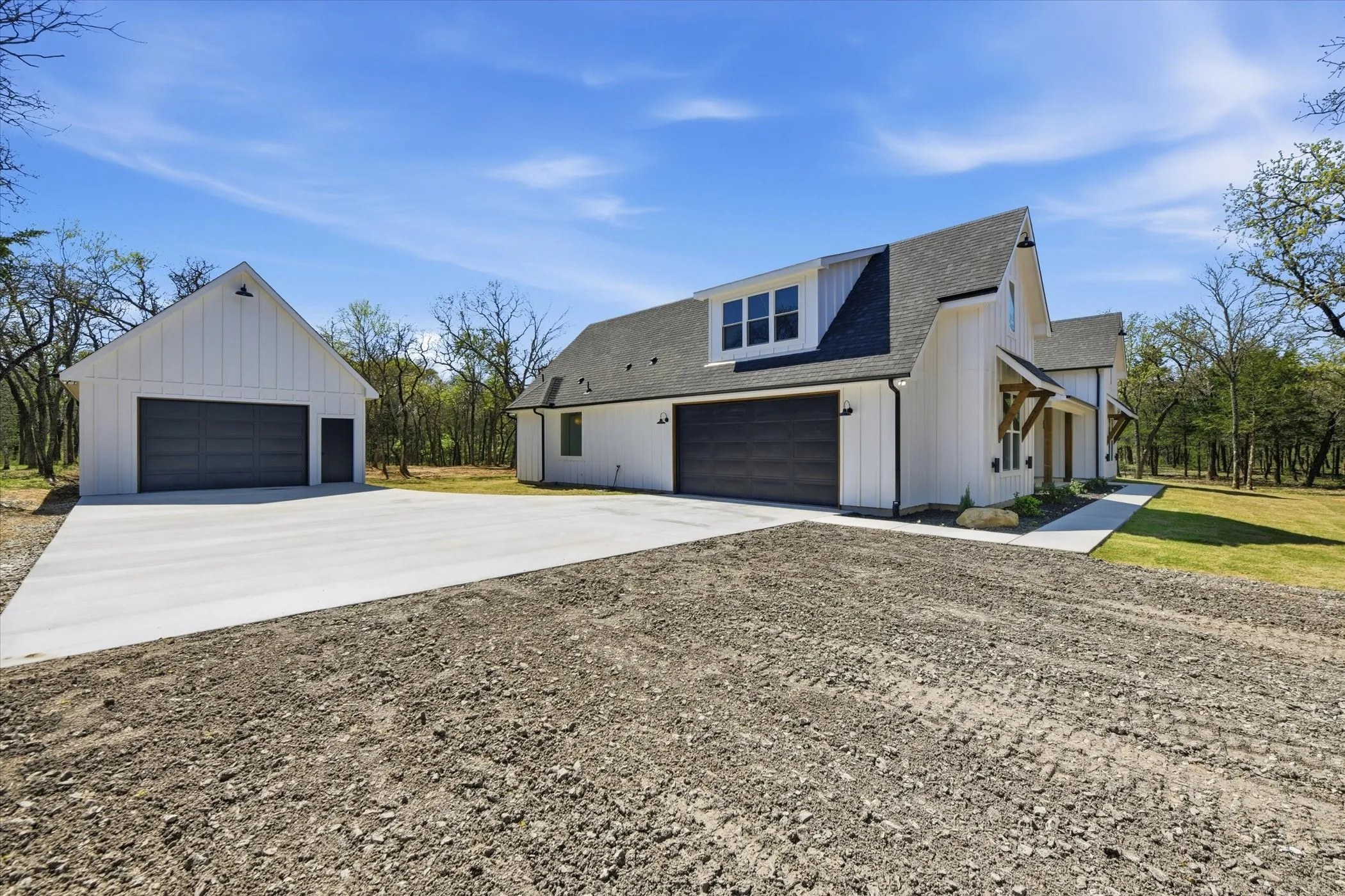 View of property exterior featuring roof with shingles, board and batten siding, a detached garage, and an outbuilding