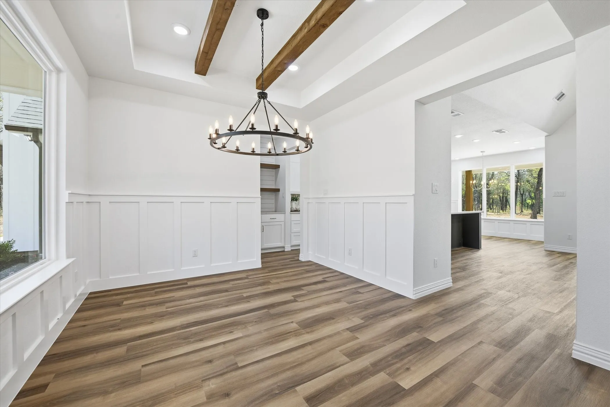 Unfurnished dining area featuring suspended lighting, beamed ceiling, a tray ceiling, wainscoting, and dark wood finished floors