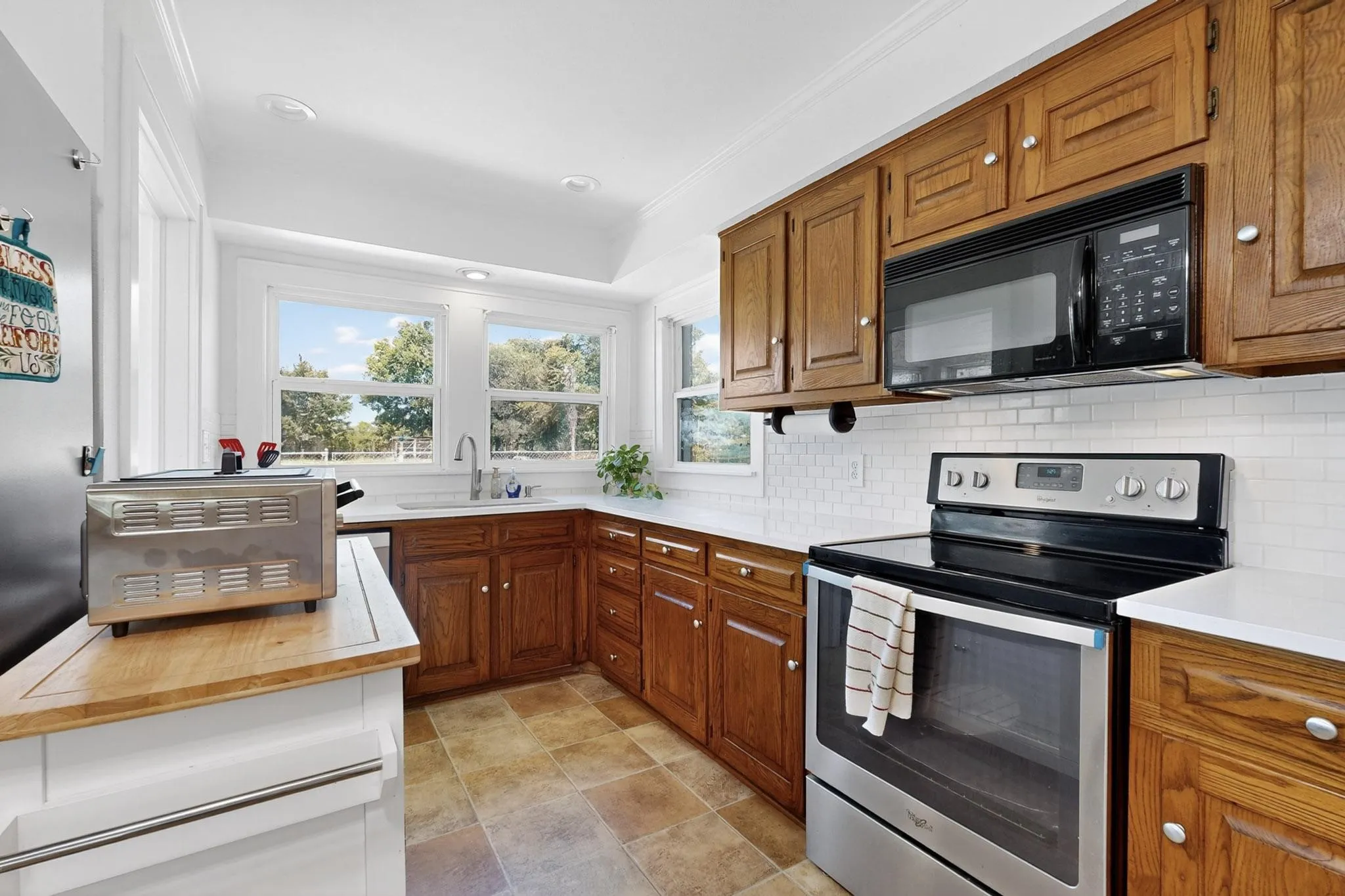 Kitchen with electric range, wood counters, brown cabinetry, black microwave, and recessed lighting