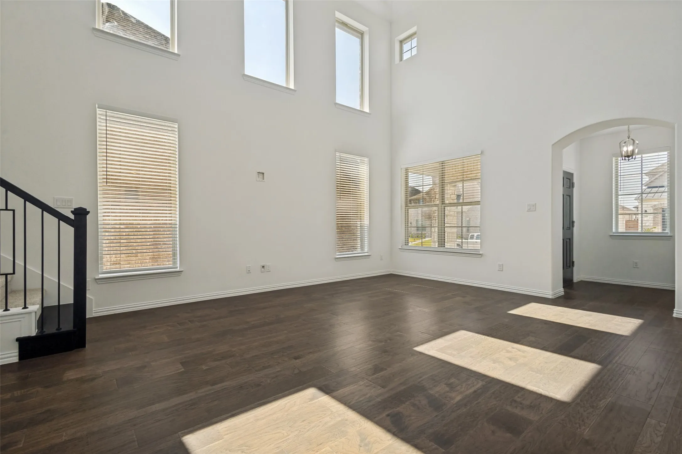 Two-story living area featuring a vaulted ceiling with multiple windows, wood-finish flooring, and a staircase with an iron railing