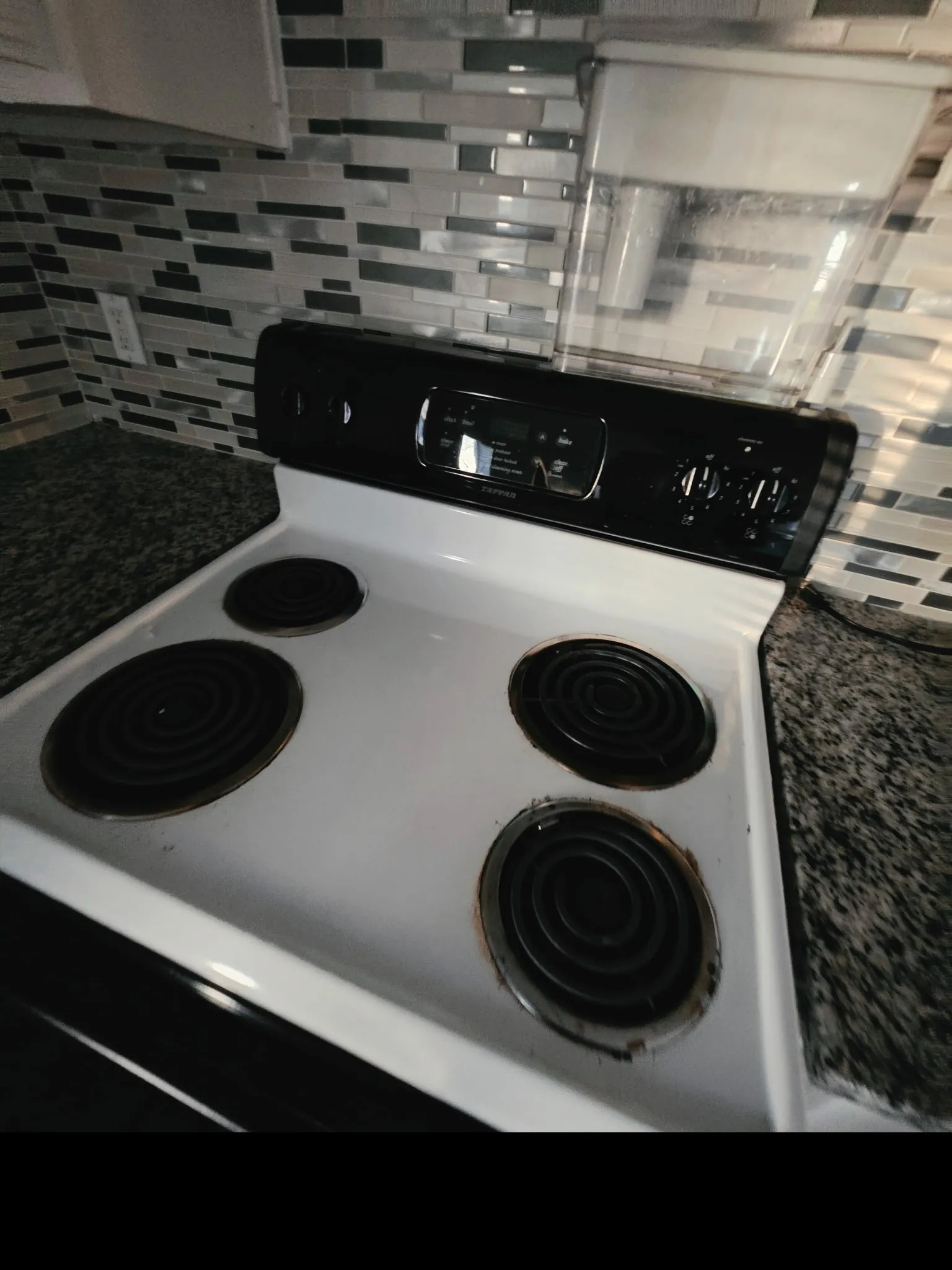 Electric range with four coil burners and control panel, complemented by a multi-tone tile backsplash