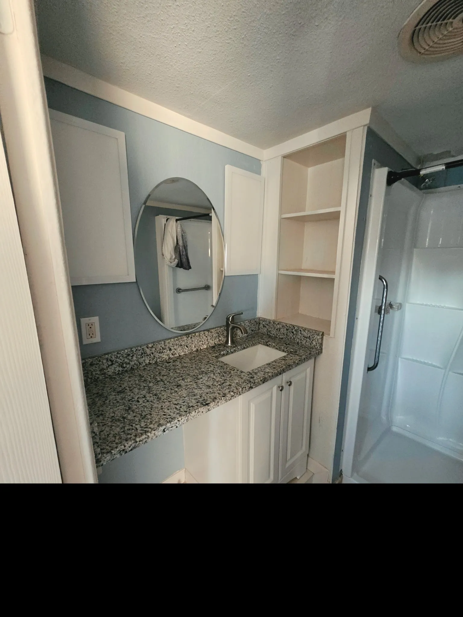 Bathroom vanity featuring a granite-finish countertop with an undermount sink, white cabinetry, and an oval mirror