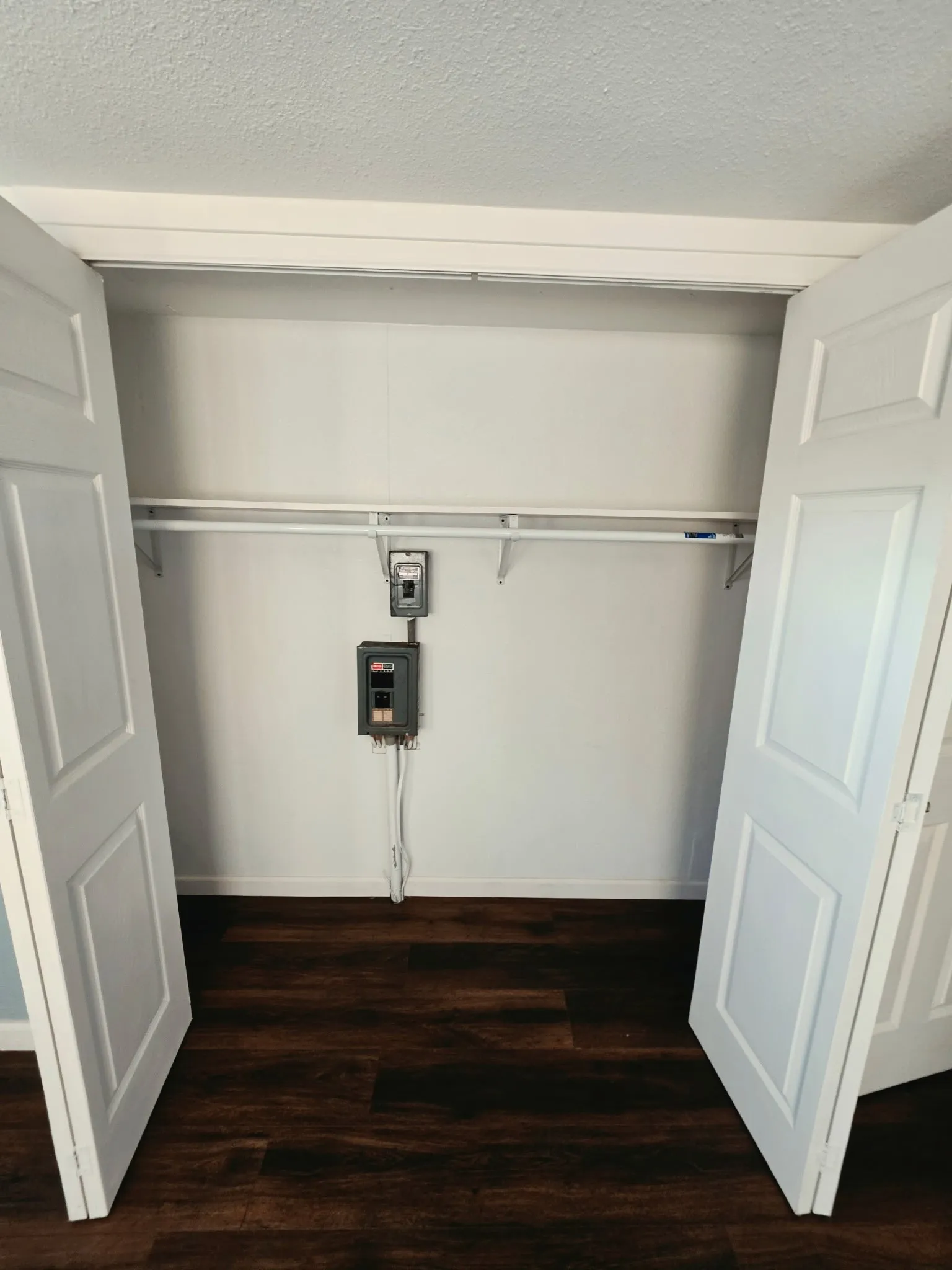 Closet space featuring white bi-fold doors, white interior walls, a white hanging rod, and dark wood-finish flooring