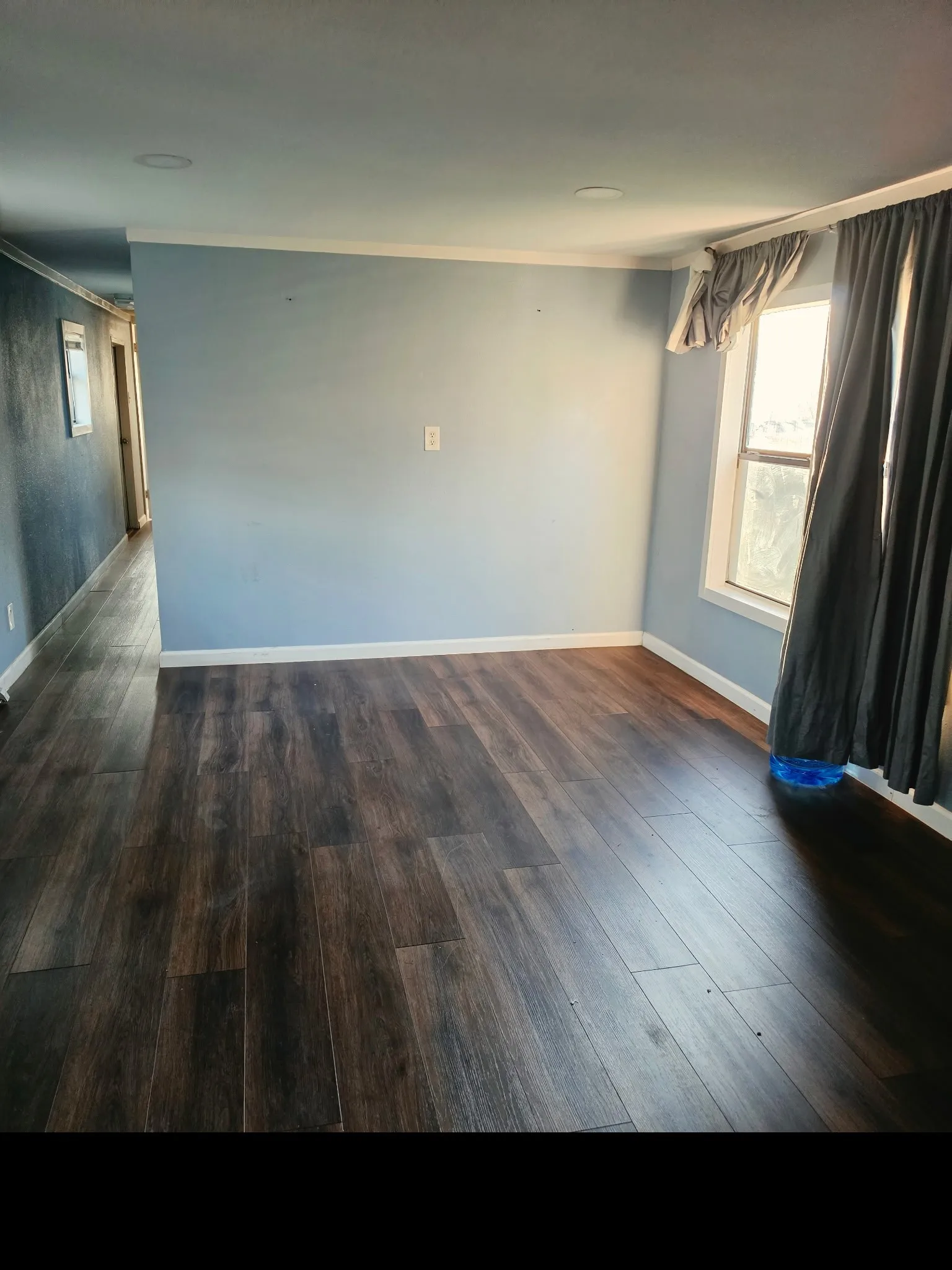 Spacious room featuring dark wood-finish flooring, light blue walls, white baseboards, and white crown molding