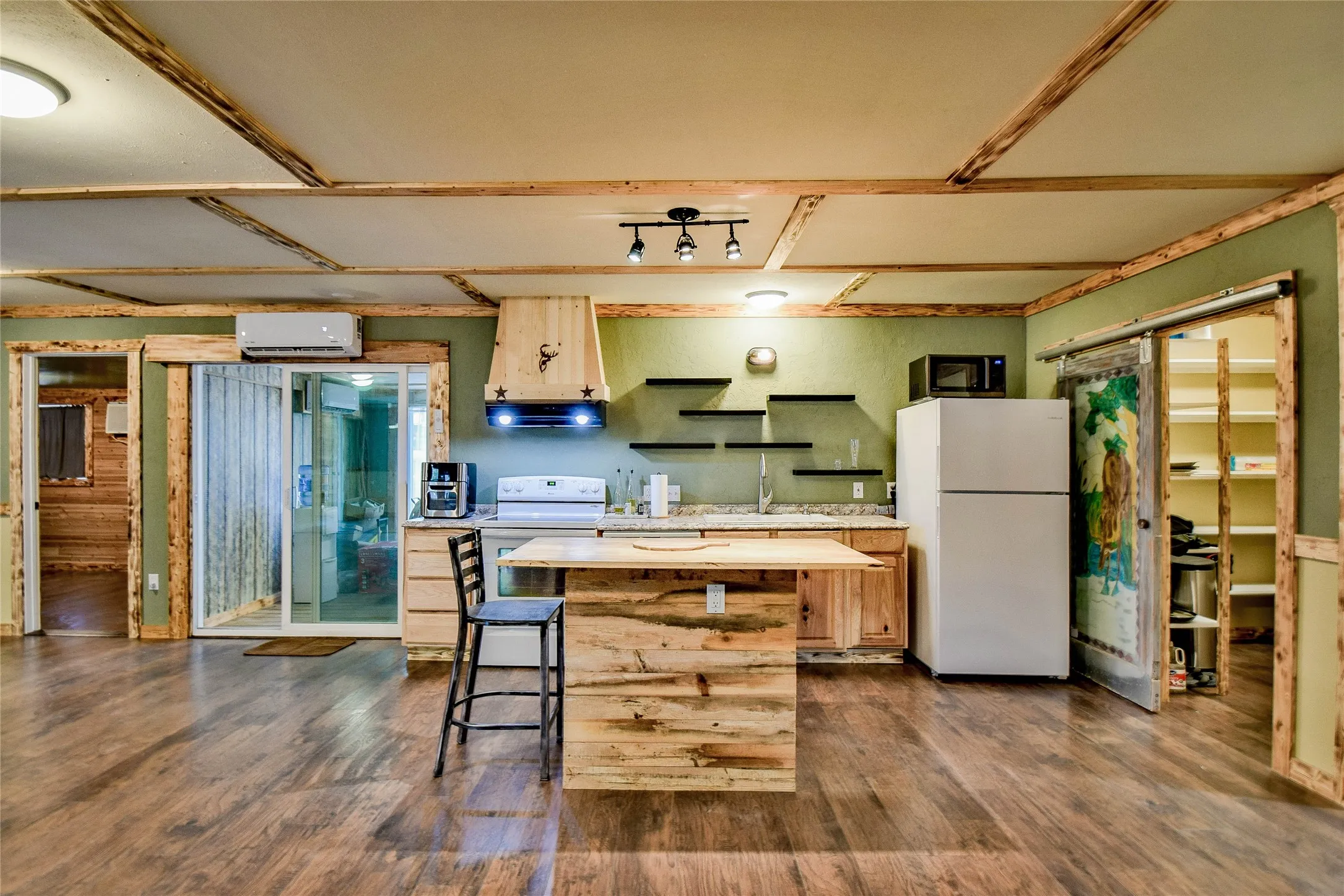 Versatile kitchen with hand-crafted ventilation hood, white appliances, great wood kitchen island, and dark wood-type laminate flooring with walk-in pantry.