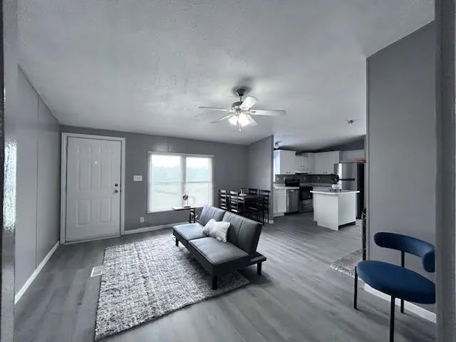Open-concept living space featuring wood-finish flooring, a ceiling fan, and a white entry door