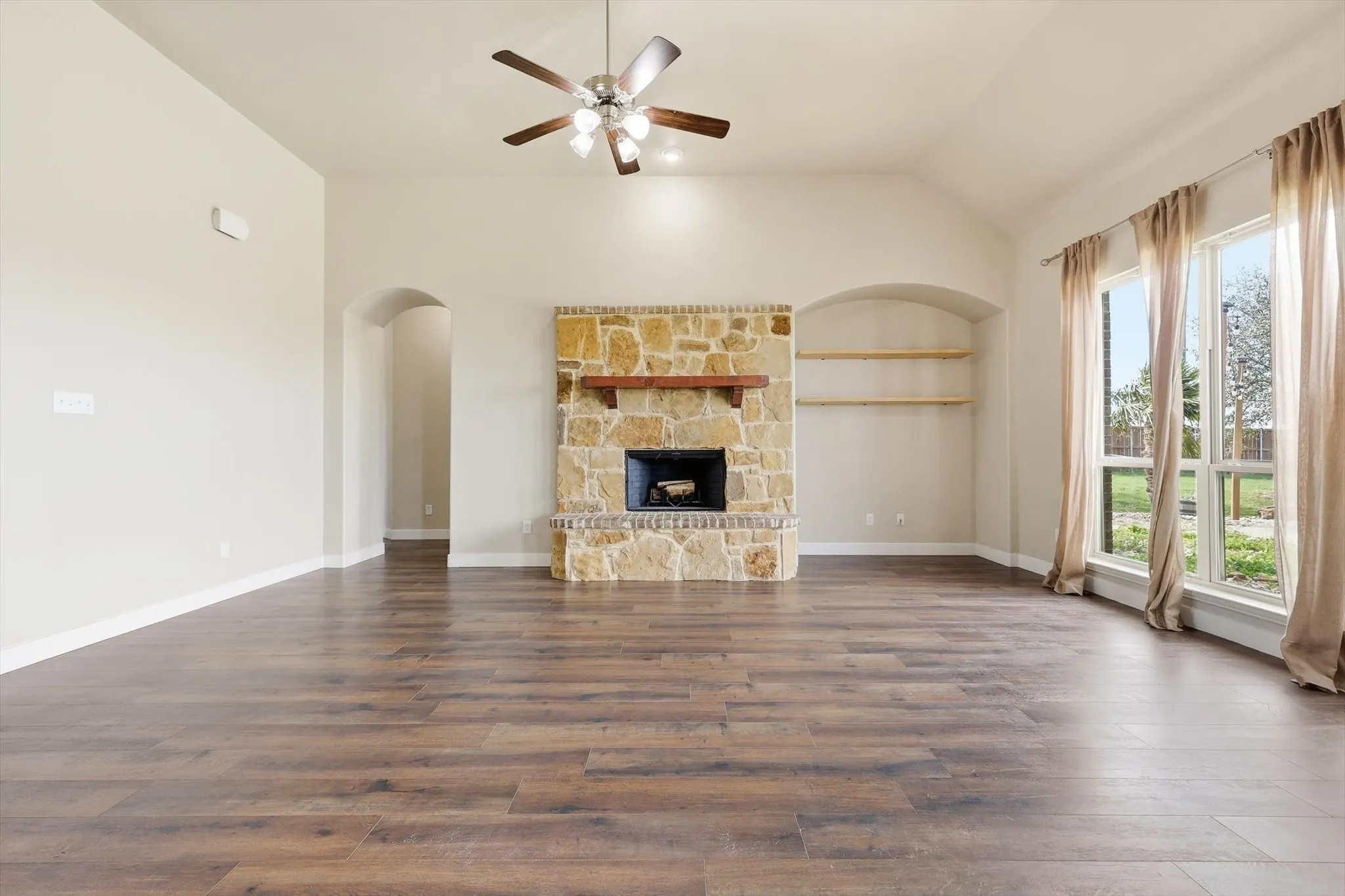 Living area with ceiling fan, arched walkways, lofted ceiling, light LVP floors, and healthy amount of natural light