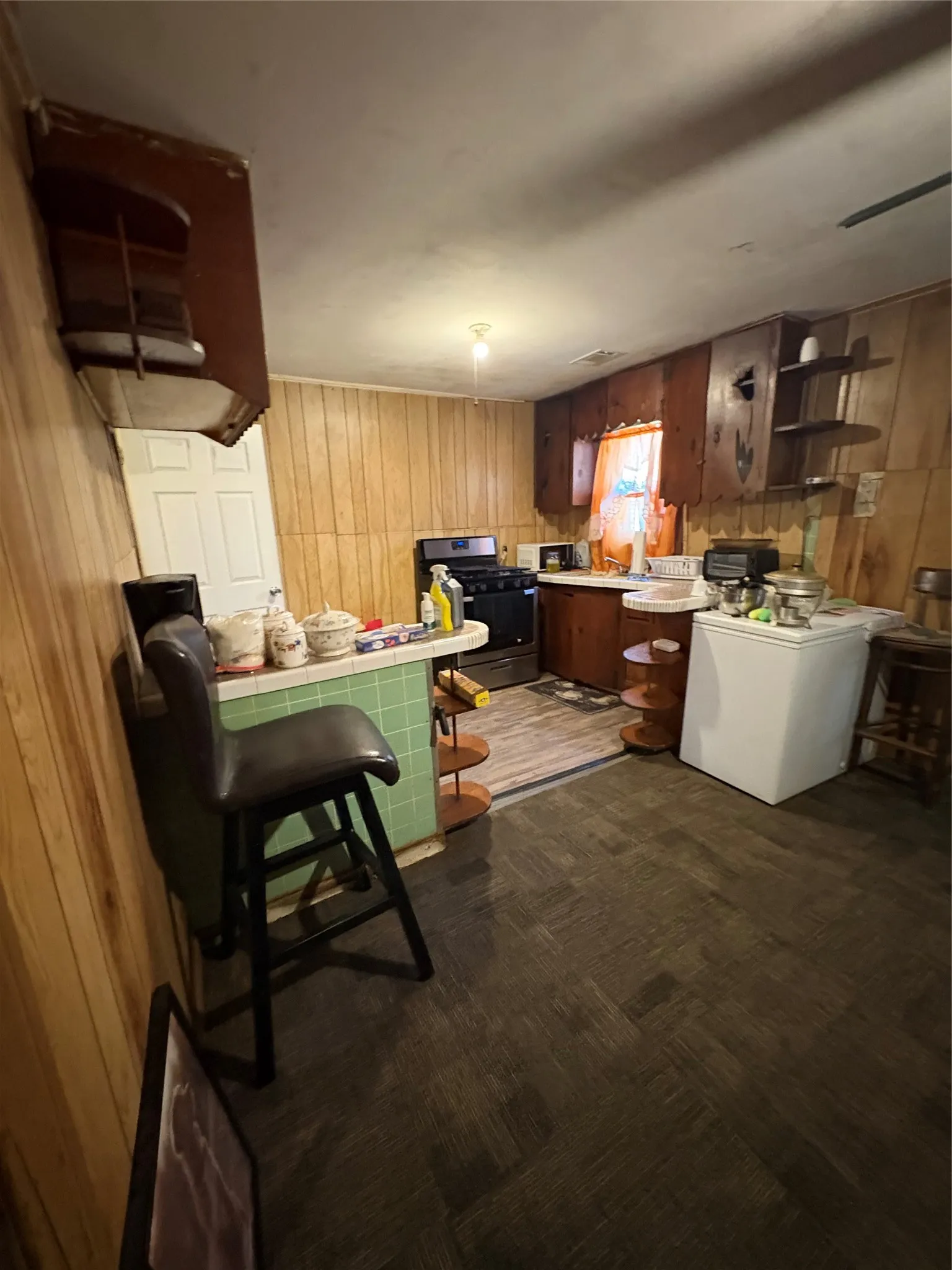Kitchen with tile countertops, wood walls, black gas stove, a peninsula, and a kitchen breakfast bar