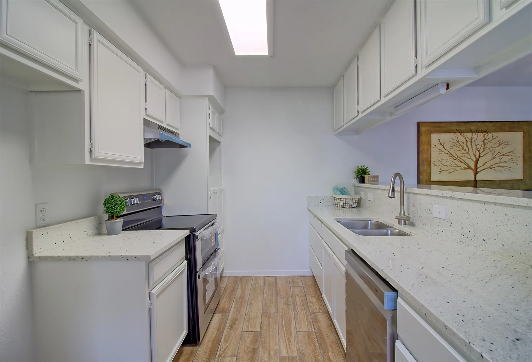 Kitchen featuring light stone countertops, stainless steel appliances, white cabinetry, and light wood-style flooring