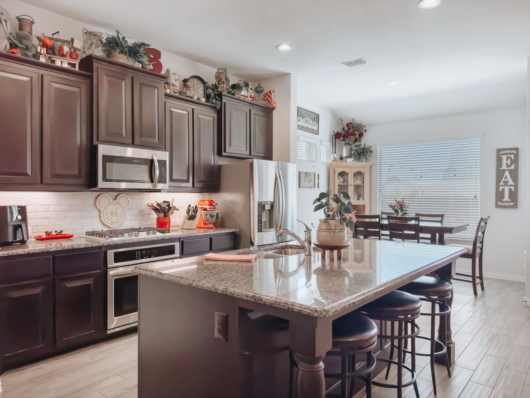 Kitchen featuring appliances with stainless steel finishes, light stone countertops, a kitchen bar, and a center island with sink