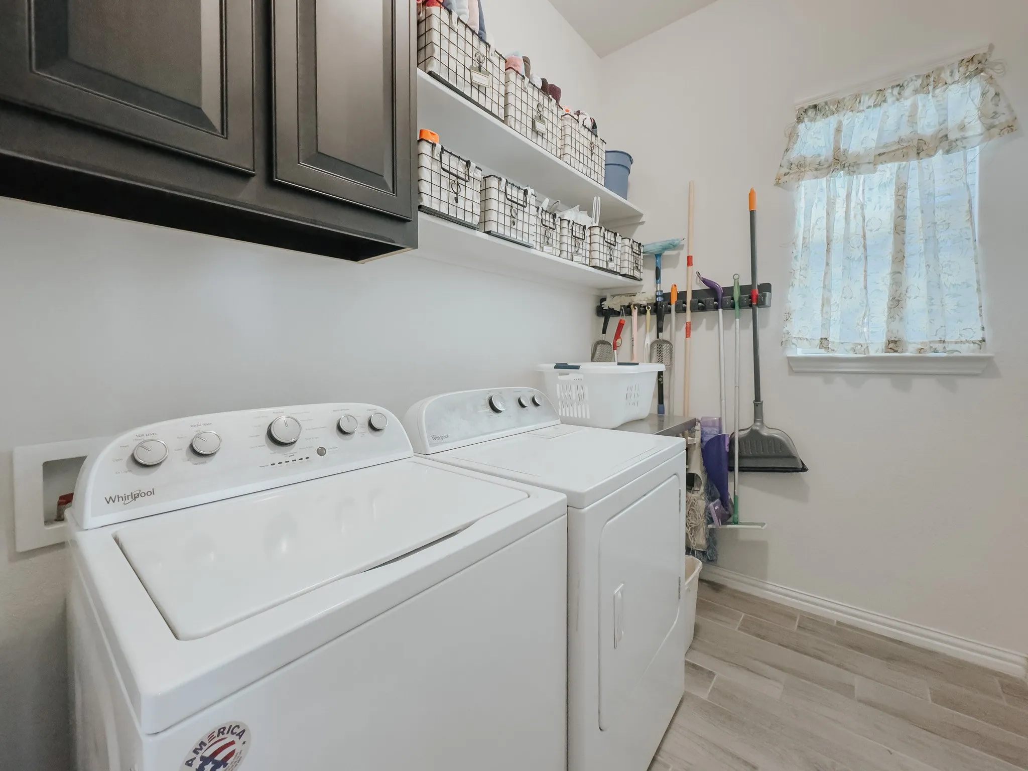 Laundry room with light floors, cabinets, and washer and clothes dryer. plus shelves with more natural light in this home