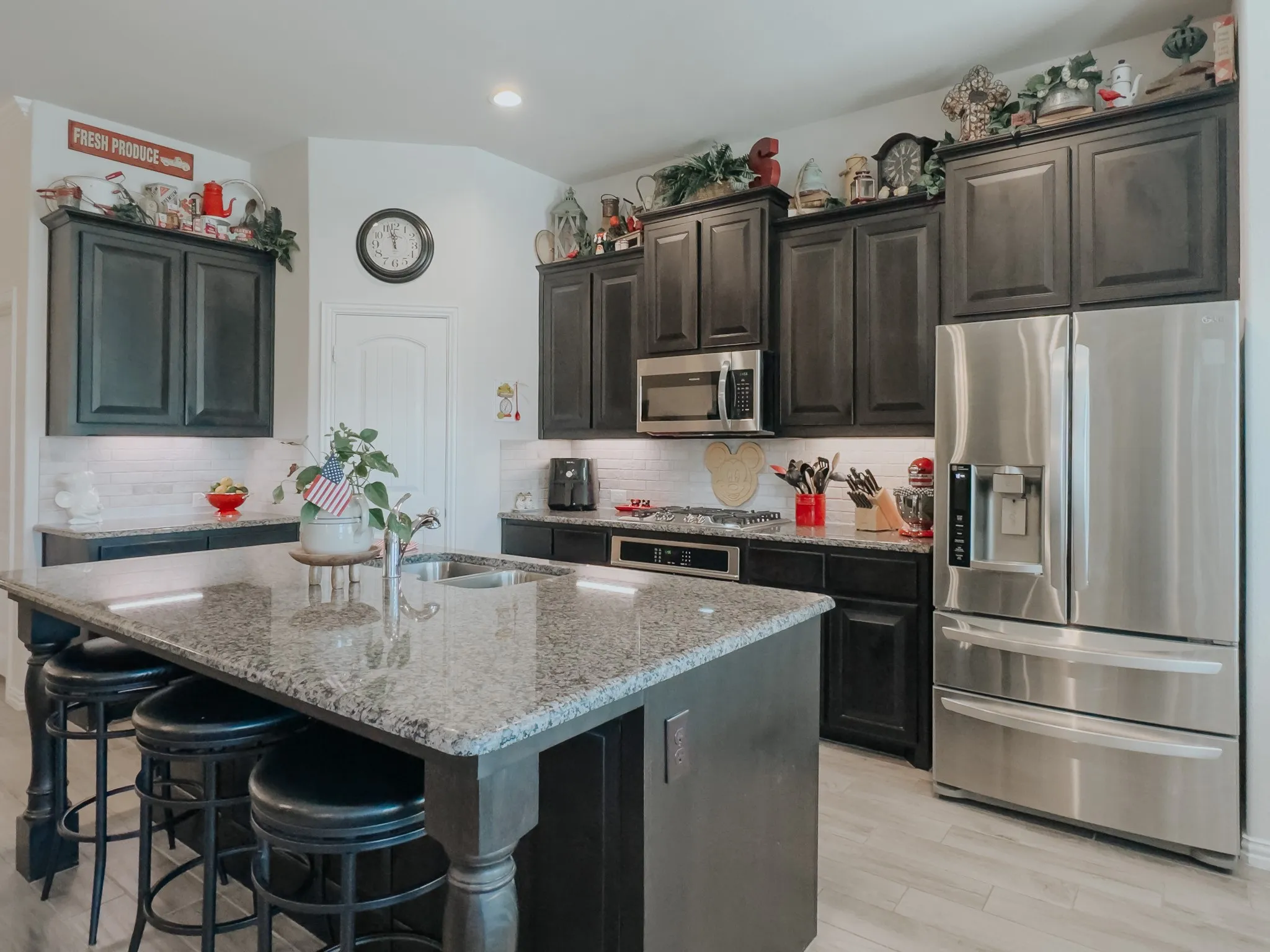 Kitchen with appliances with stainless steel finishes, light colored floors, tasteful backsplash, a kitchen island with sink, and light stone countertops