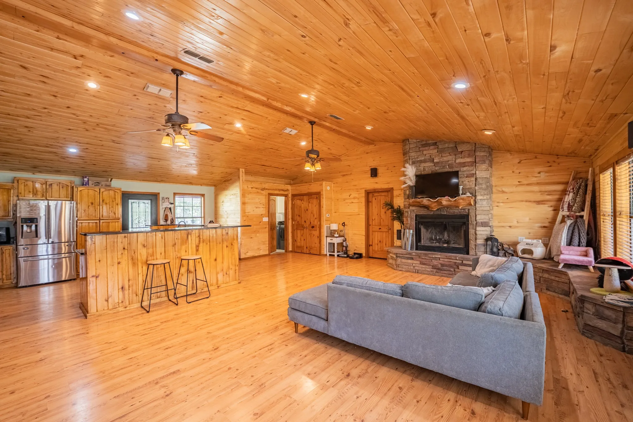 Living room featuring vaulted ceiling, light wood-type flooring, a ceiling fan, recessed lighting, and a stone fireplace