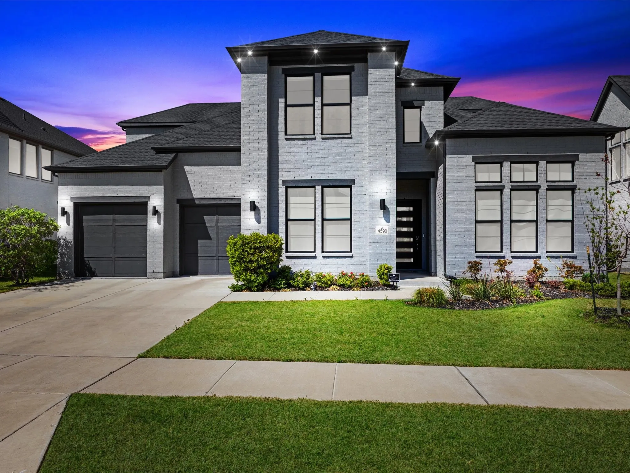 Contemporary home with a garage, a yard, concrete driveway, brick siding, and a shingled roof