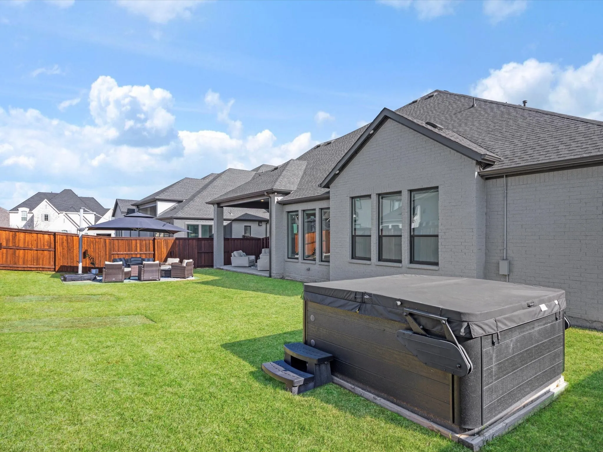Back of property featuring an outdoor living space, a patio, a hot tub, a fenced backyard, and brick siding