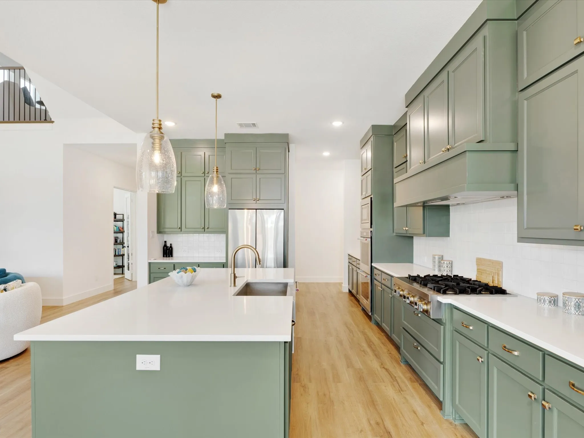 Kitchen with green cabinets, stainless steel appliances, an island with sink, and light wood-type flooring