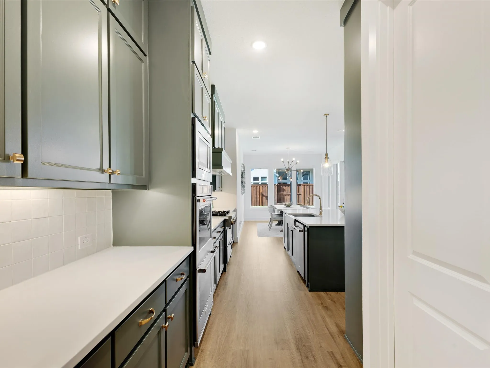 Kitchen with light wood finished floors, a center island with sink, stainless steel appliances, light stone countertops, and hanging lights
