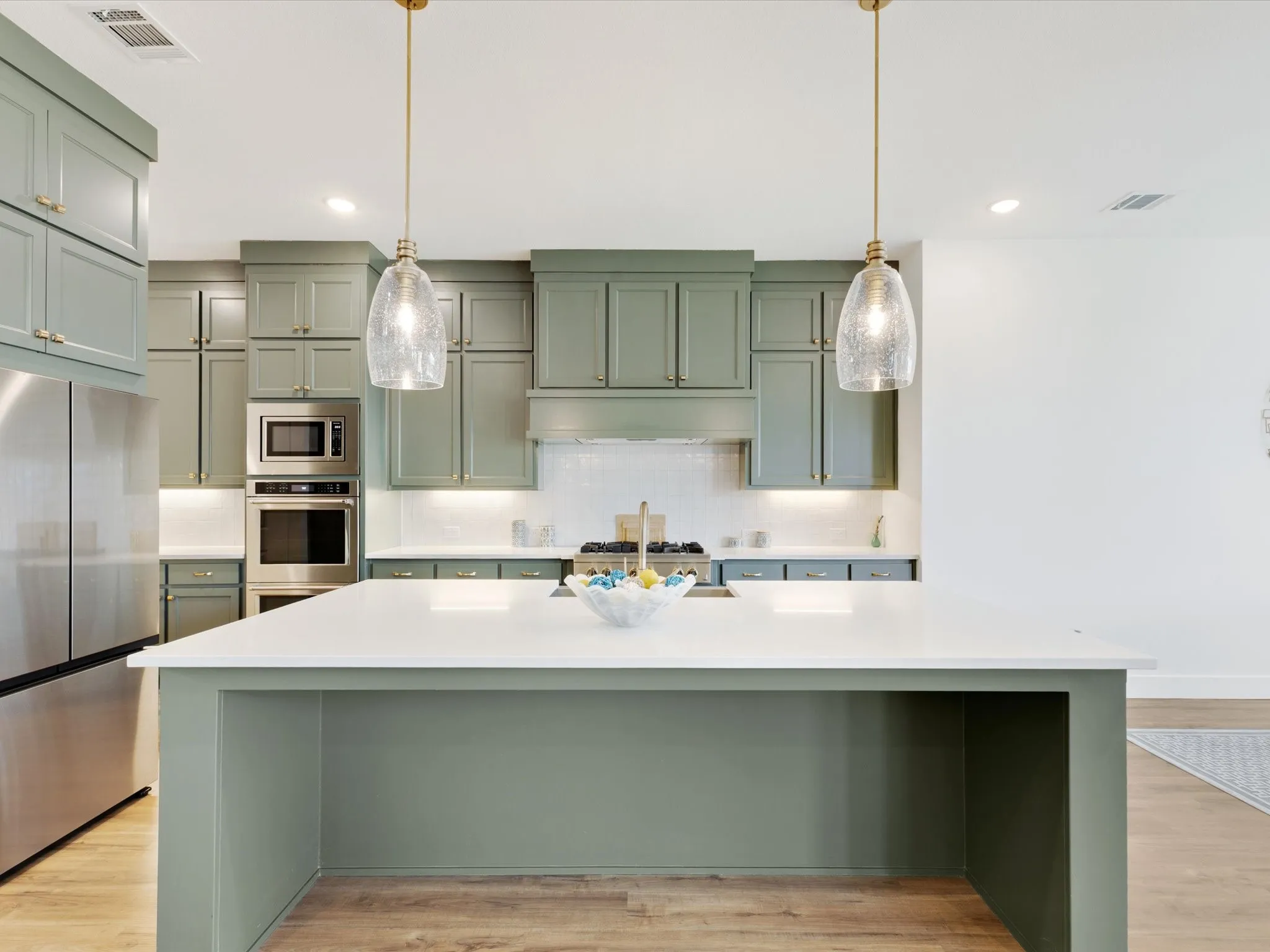 Kitchen featuring stainless steel appliances, an island with sink, light wood-style flooring, and green cabinets