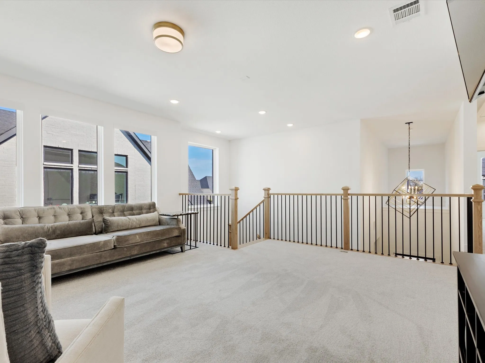 Living area with carpet flooring, suspended lighting, and an upstairs landing