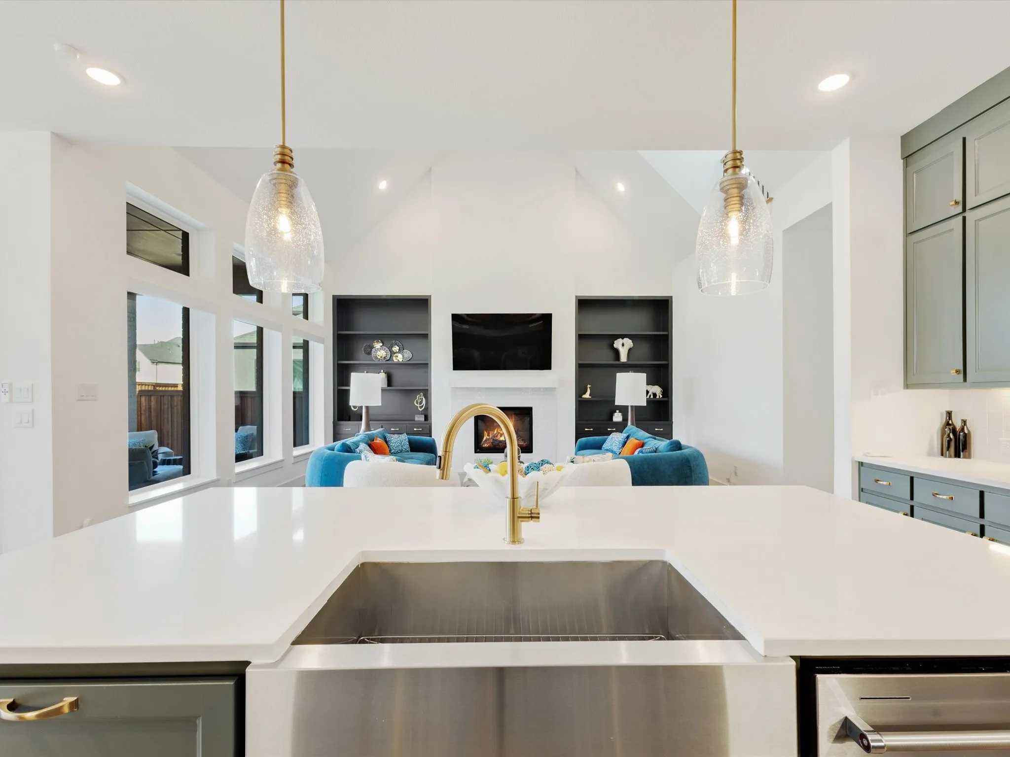 Kitchen featuring open floor plan, a lit fireplace, decorative light fixtures, vaulted ceiling, and an island with sink